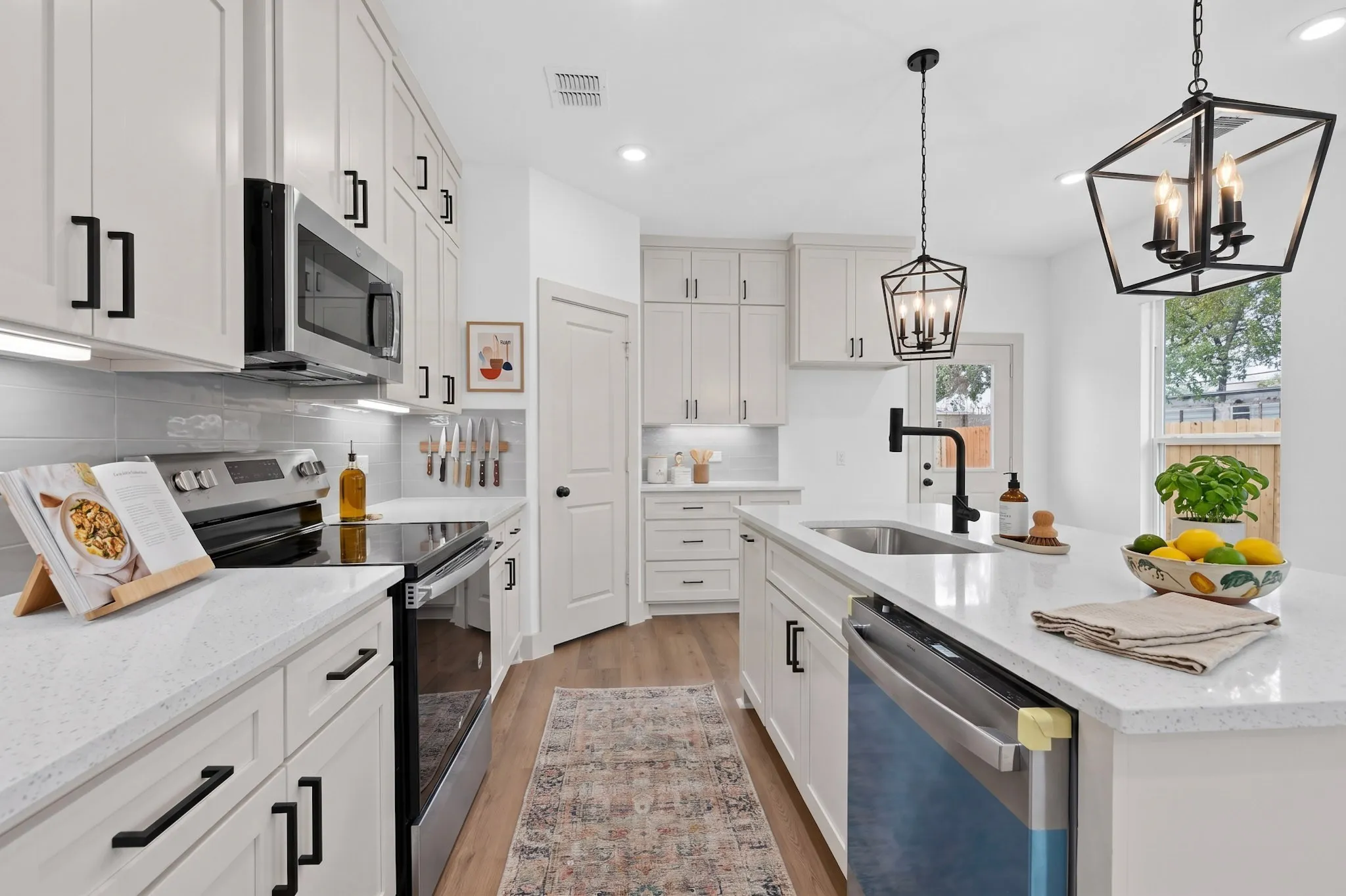 (Virtual Staging)White shaker cabinetry, light-toned countertops, stainless steel appliances, wood-finish flooring, and black hardware