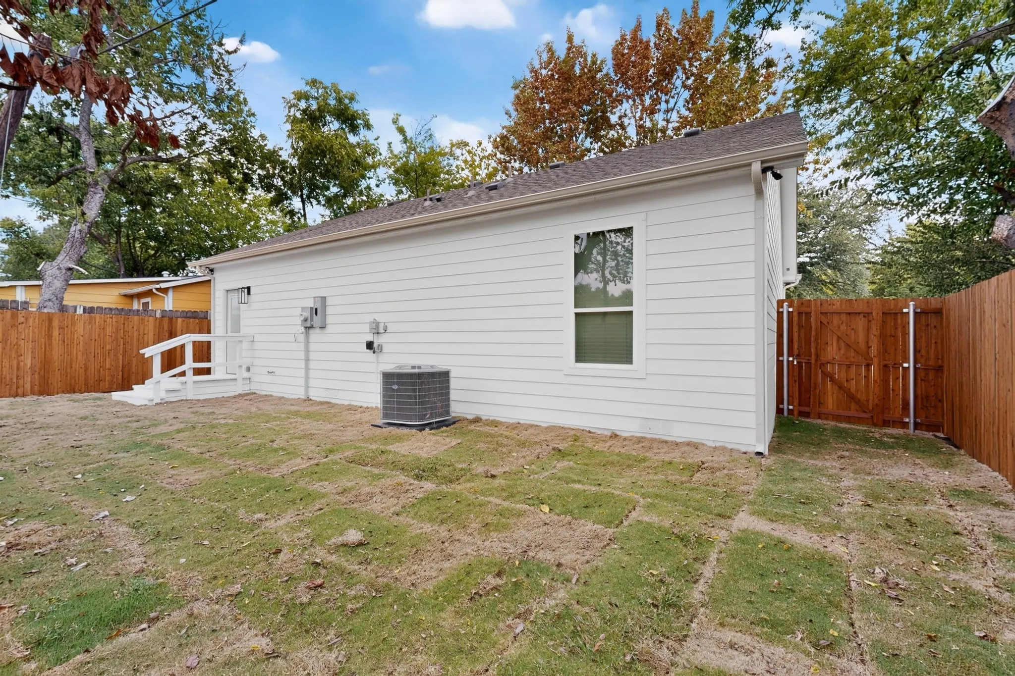 White siding exterior with a brown shingled roof, featuring a white rear deck with railing, a brown privacy fence, and a wooden gate
