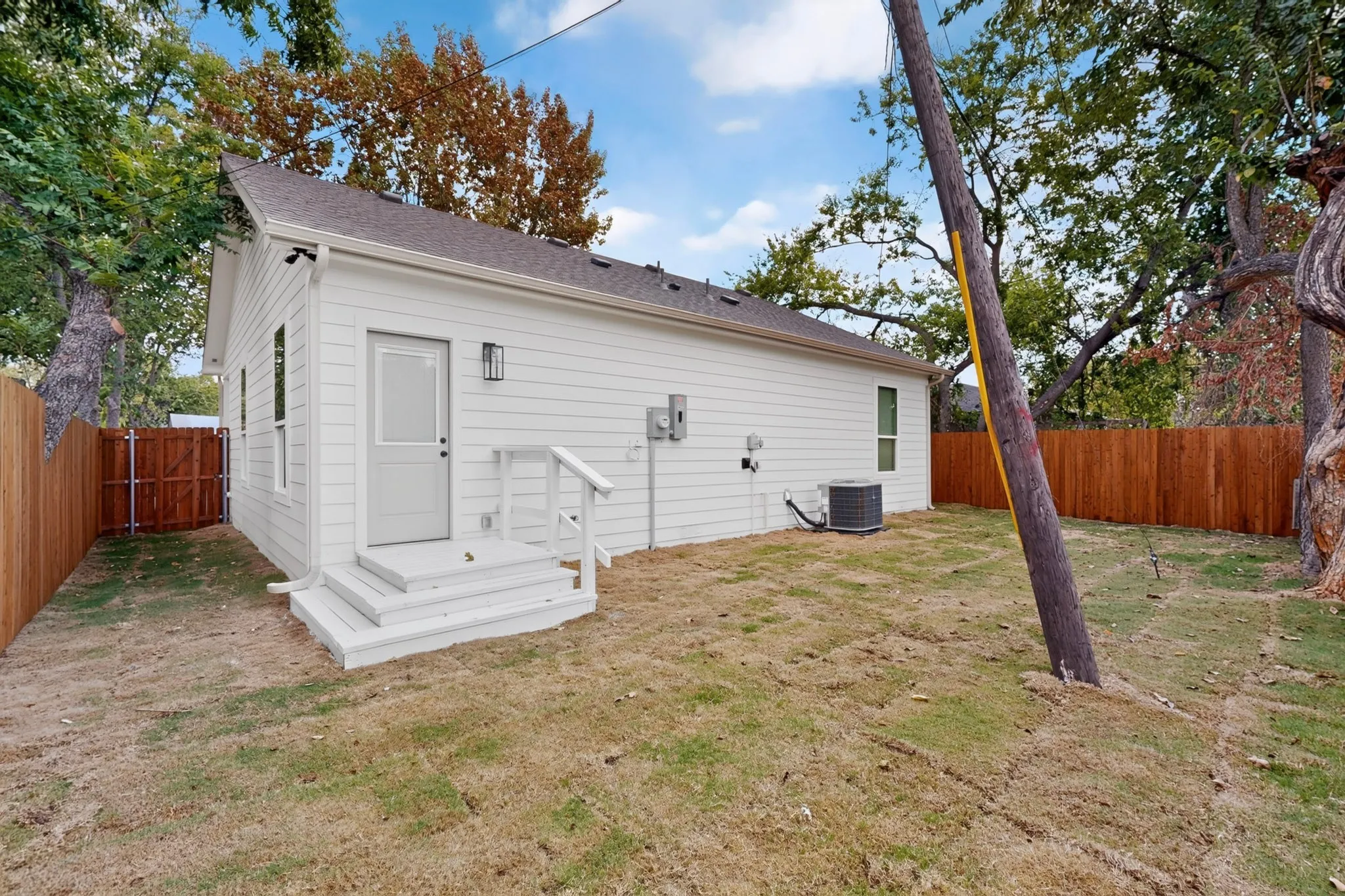 White horizontal siding with a dark roof and a brown wooden privacy fence