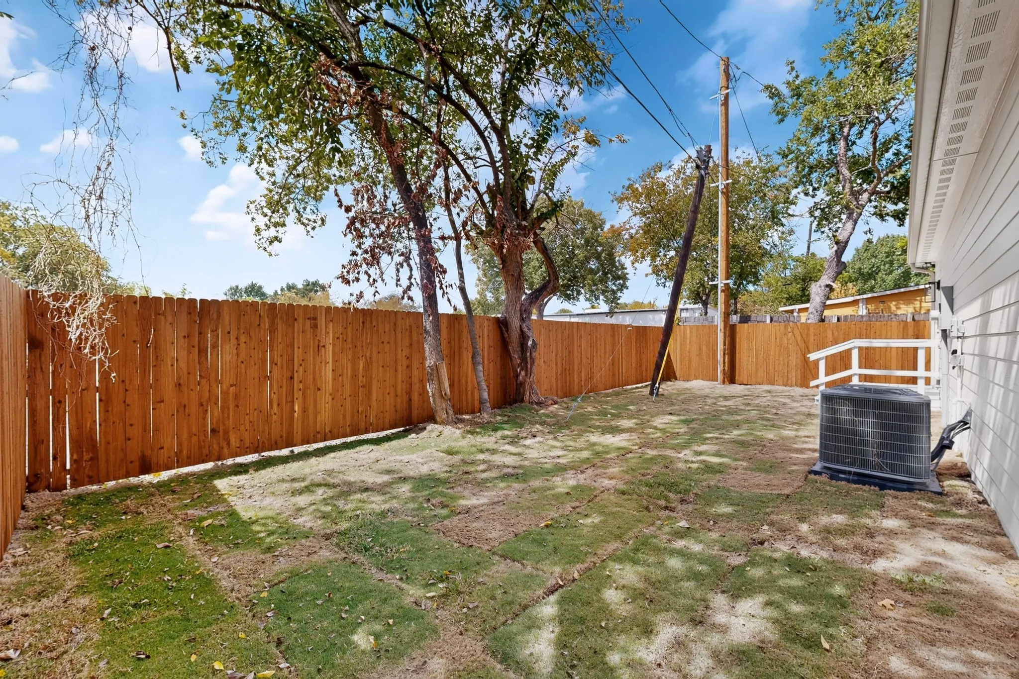 Expansive rear yard featuring a wood privacy fence, mature trees, and a manicured lawn