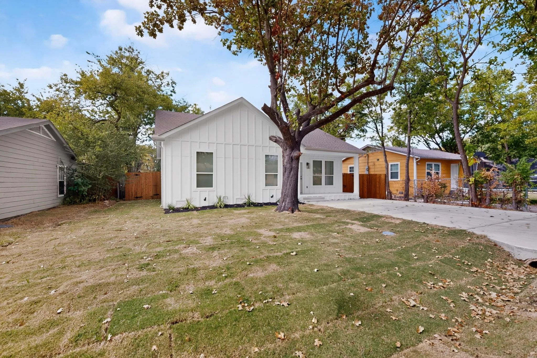 White board-and-batten exterior, concrete driveway, front yard with mature tree, fenced side yard, and a single-story architectural design