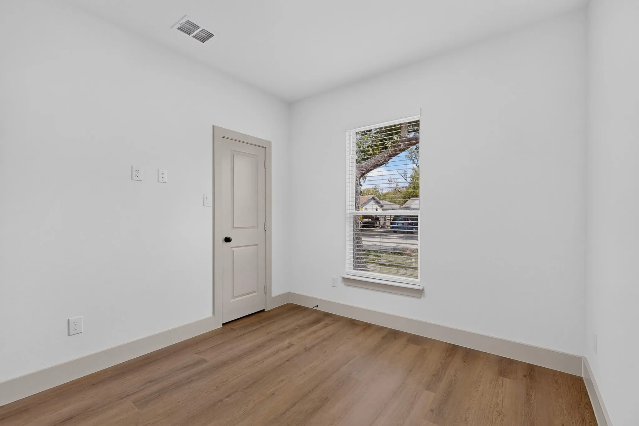 Wood-finish flooring, white walls, and a window with blinds