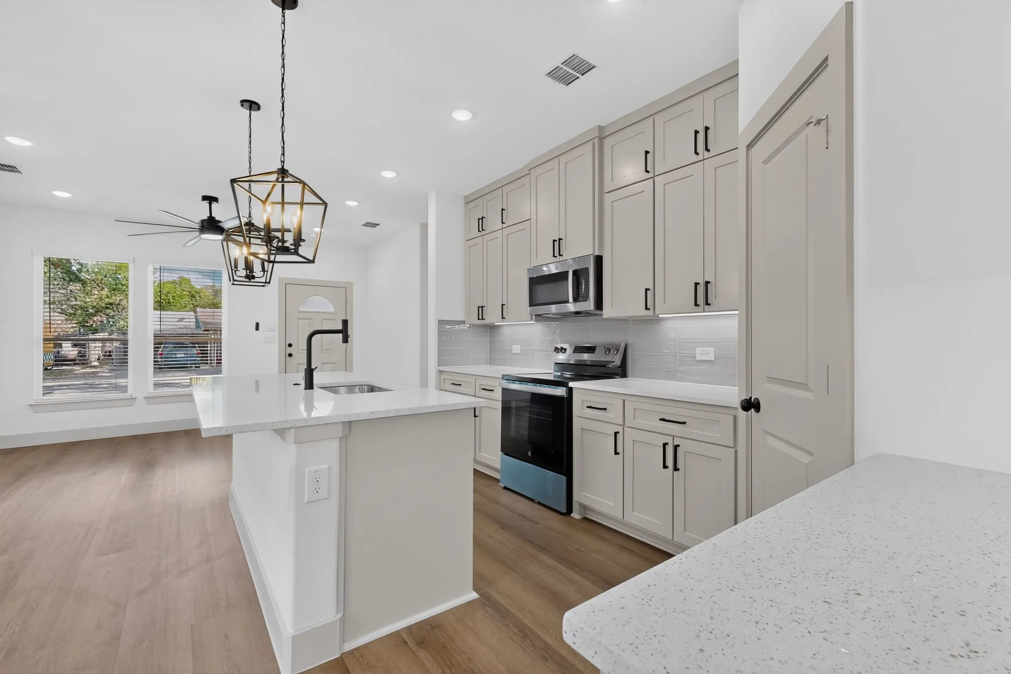Kitchen featuring light-toned cabinetry, stainless steel appliances, a white tile backsplash, and an island with a contrasting countertop