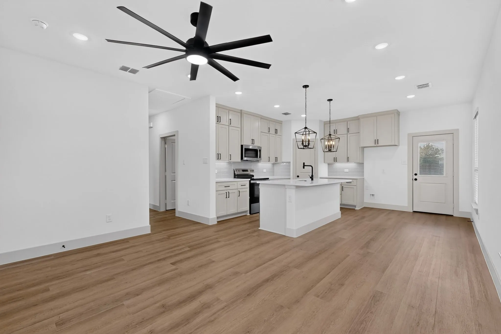 Open-concept space featuring wood-finish flooring, a modern ceiling fan, recessed lighting, and a kitchen with an island, pendant lighting, and light-toned cabinetry