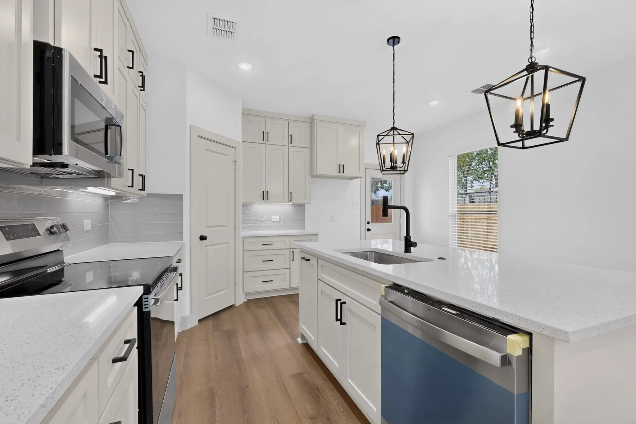 Contemporary kitchen featuring white cabinetry, light-toned countertops, stainless steel appliances, and wood-finish flooring