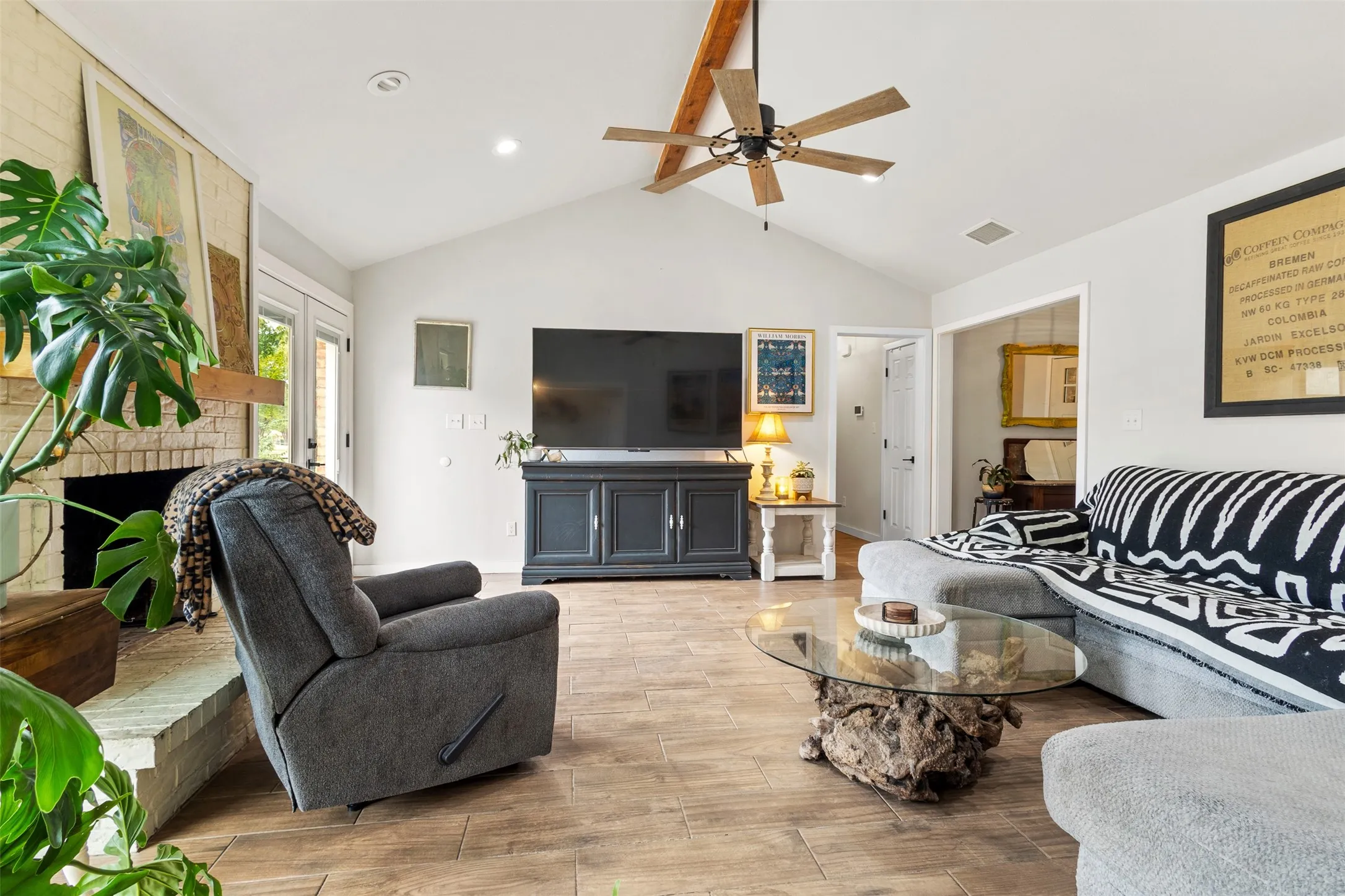 Vaulted ceiling with exposed wood beam, wood-finish flooring, brick fireplace with wood mantel, ceiling fan with integrated lighting, recessed lighting