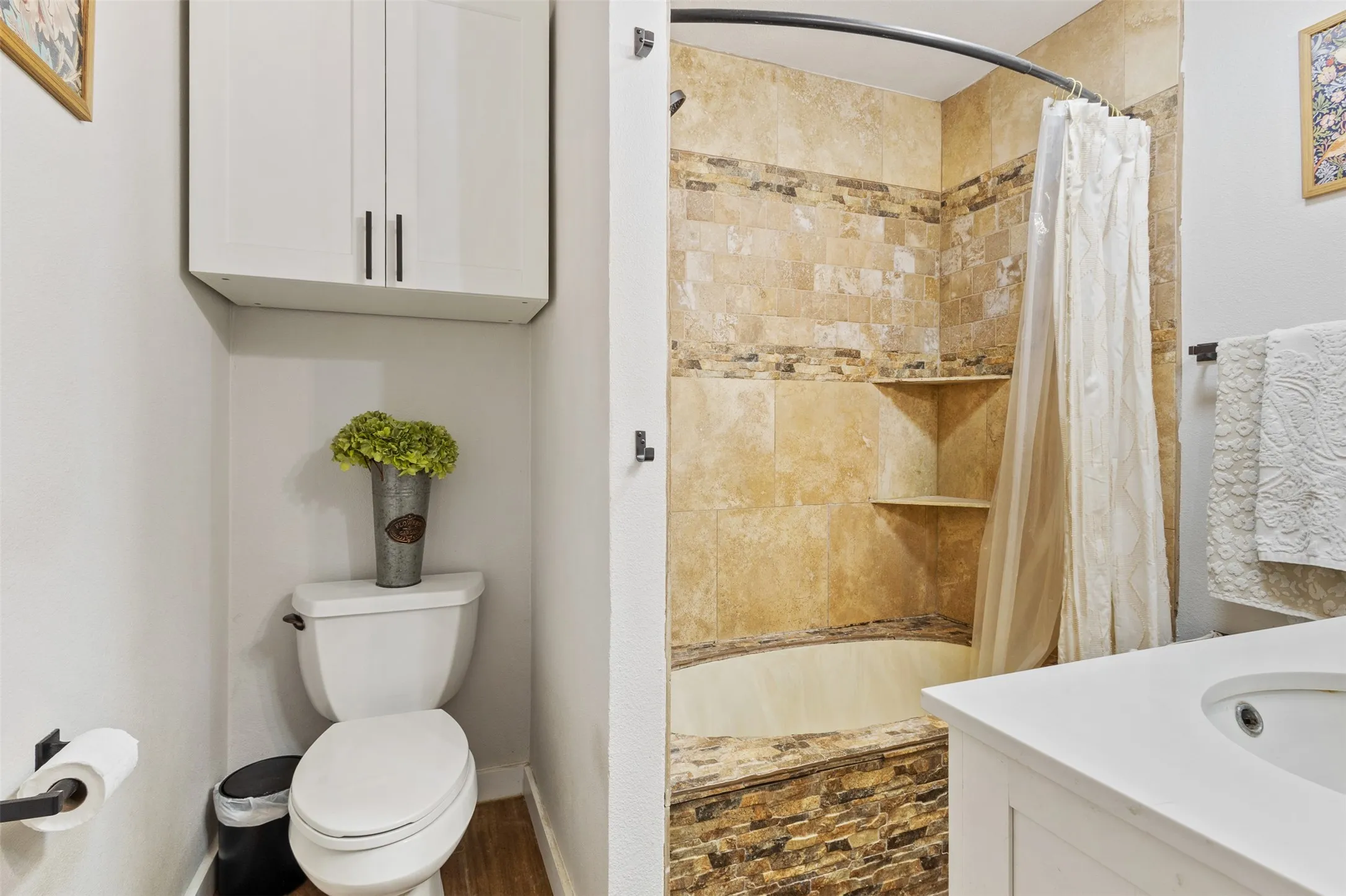 Bathroom featuring a tiled shower with integrated shelving, built-in bathtub, white vanity with an undermount sink, and overhead cabinetry