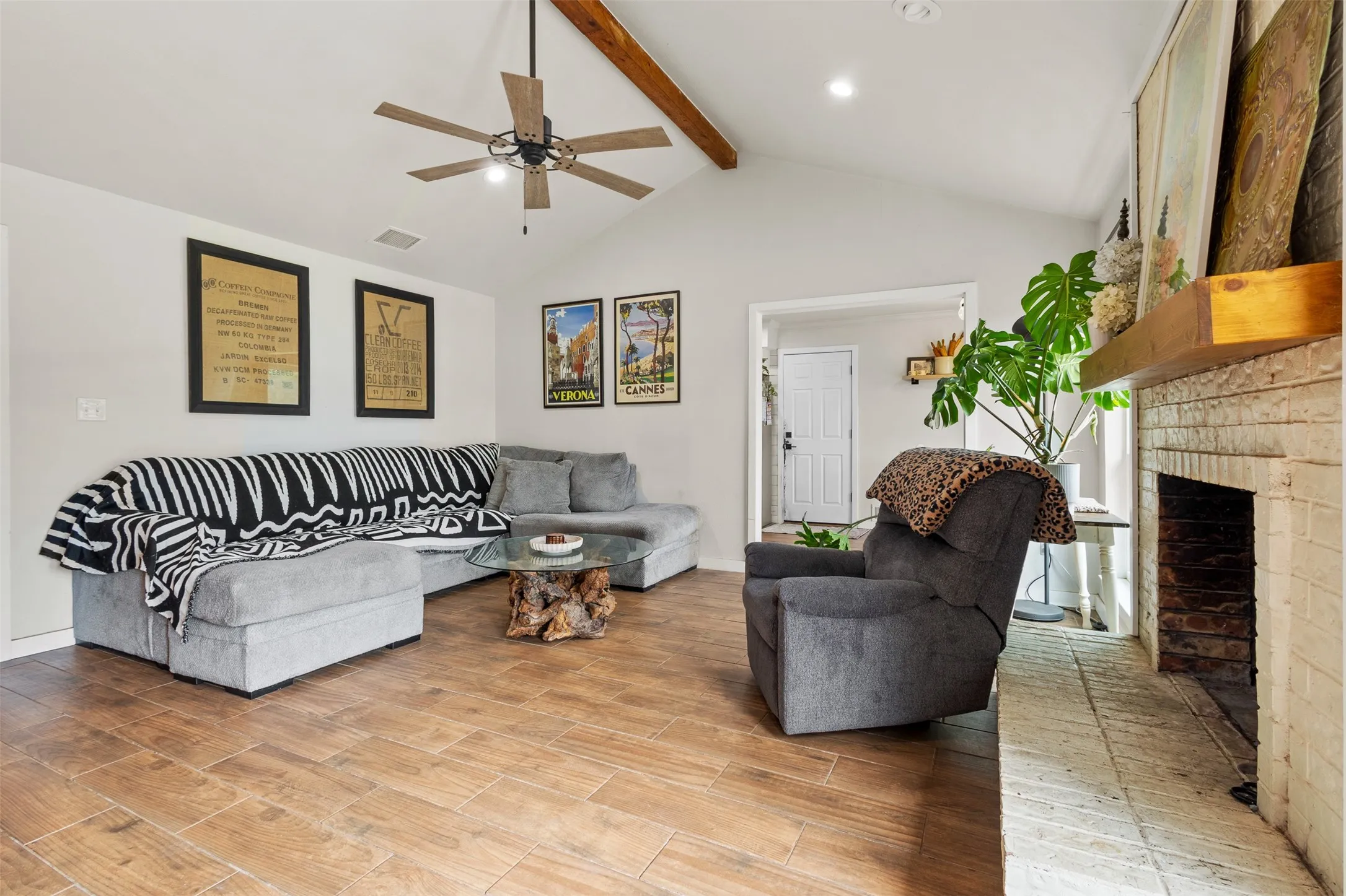 Vaulted ceiling with exposed wood beam, wood-finish flooring, recessed lighting, ceiling fan, and brick fireplace with wood mantel