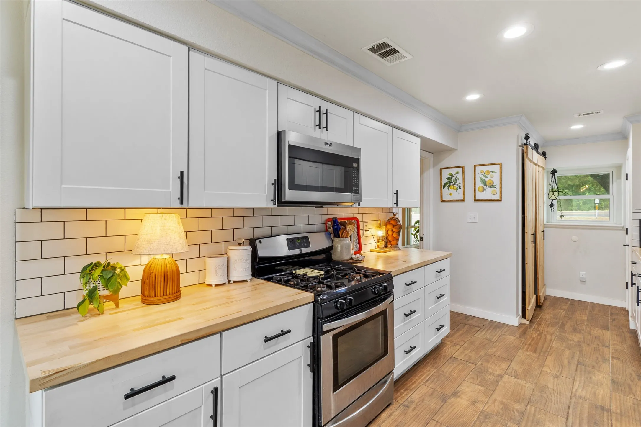 White shaker cabinetry, wood-finish countertops, stainless steel appliances, subway tile backsplash, and wood-finish flooring