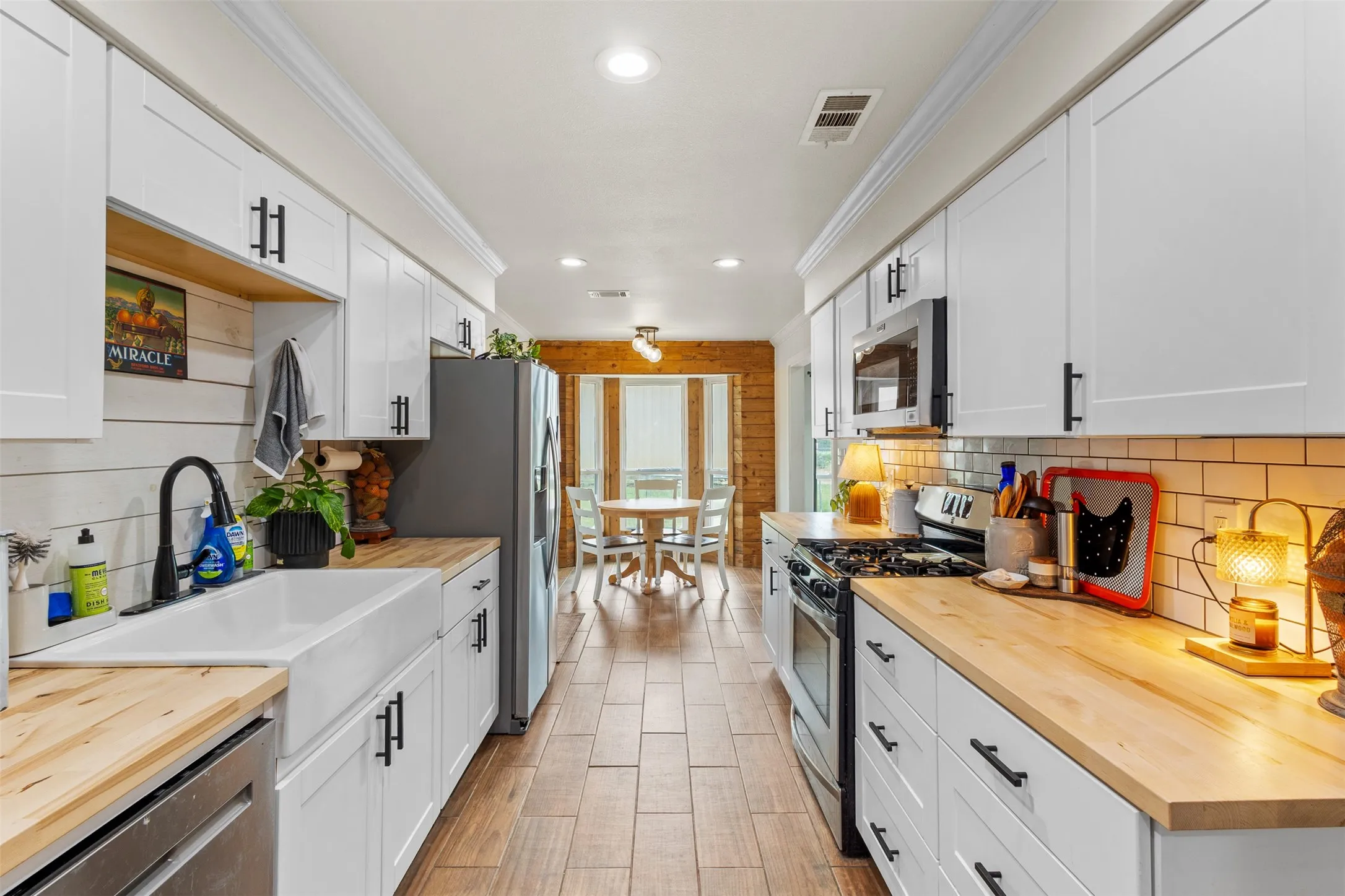 Galley kitchen featuring white cabinetry, butcher block countertops, stainless steel appliances, a farmhouse sink, and wood-look tile flooring