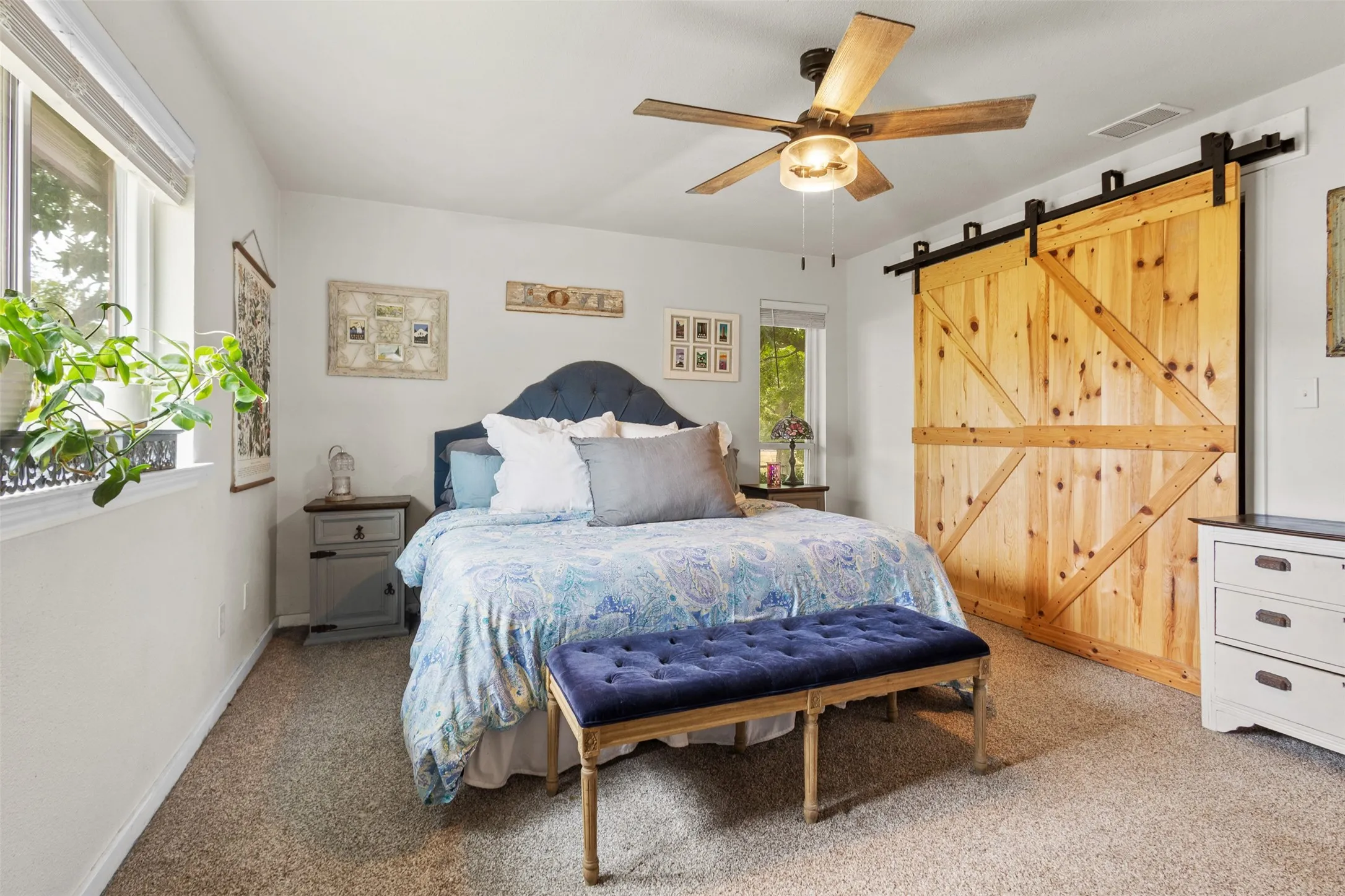 Light-colored walls, ceiling fan with light fixture, carpeted flooring, and a large wood barn door