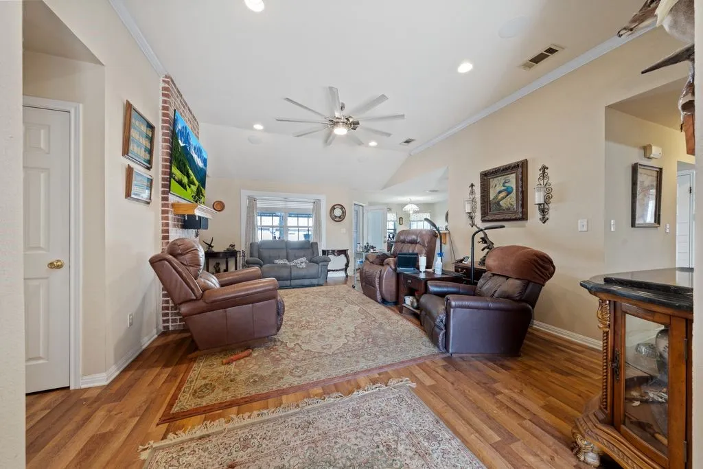 Vaulted ceiling with a ceiling fan, recessed lighting, wood-finish flooring, and a brick-finish fireplace