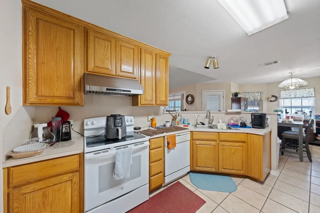 Kitchen featuring wood cabinetry, white appliances, a stainless steel range hood, and tile flooring