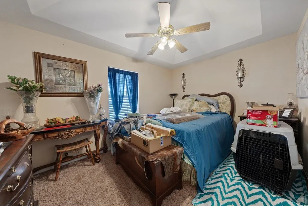 Tray ceiling with a ceiling fan, wall-mounted sconces, and carpeted flooring