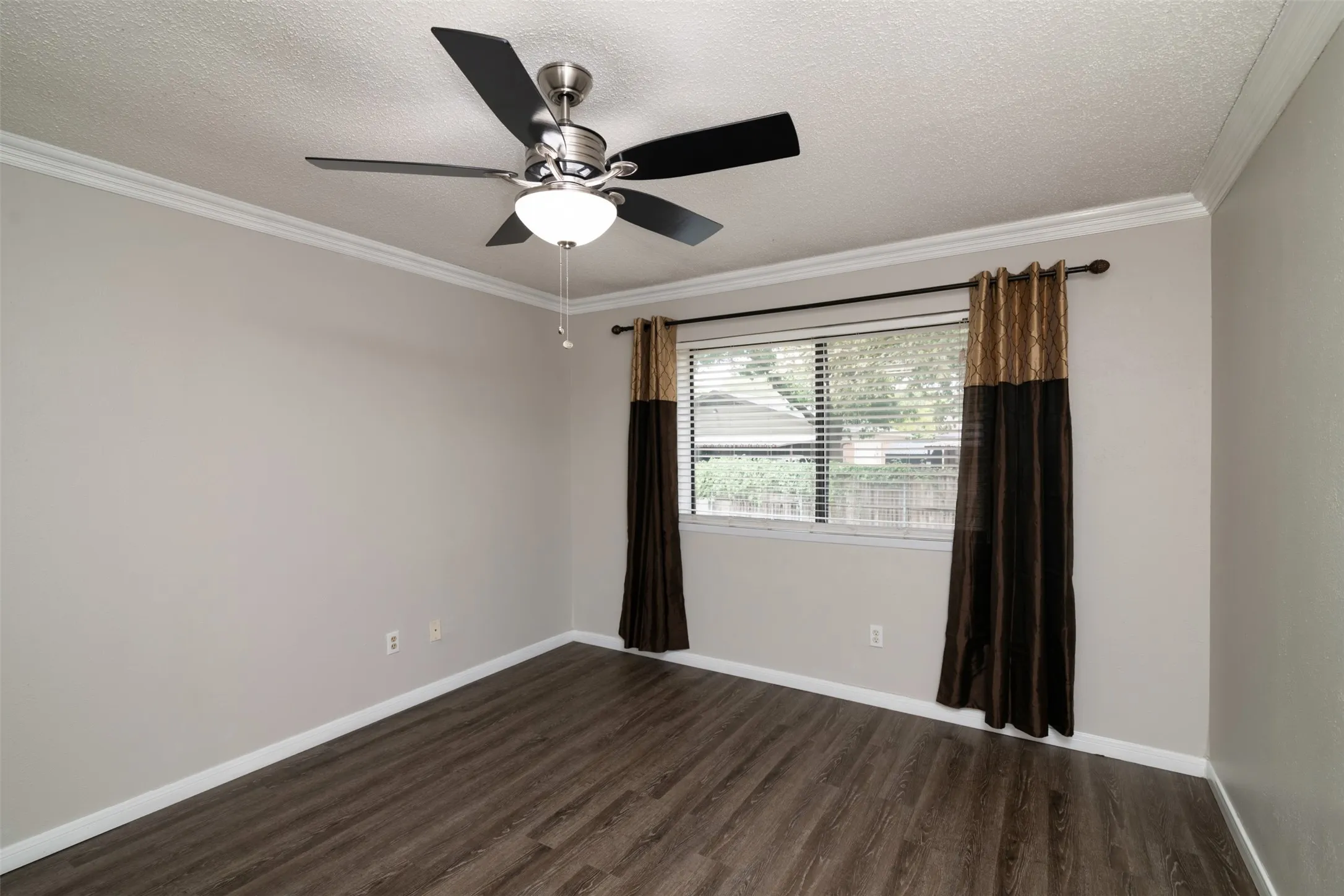 Wood-finish flooring with crisp white baseboards, crown molding, and a ceiling fan with integrated lighting