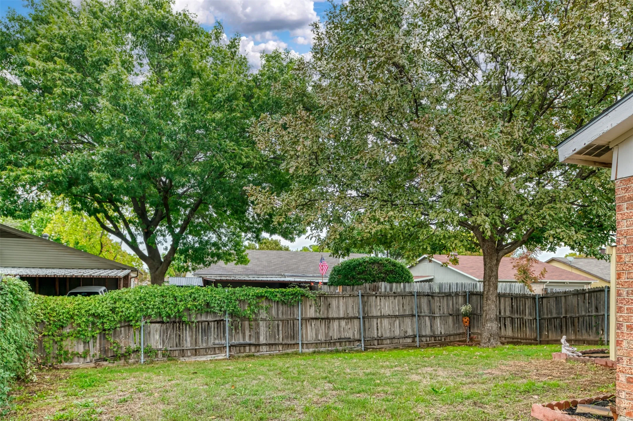 Expansive backyard featuring a manicured lawn, mature trees, and a wooden privacy fence