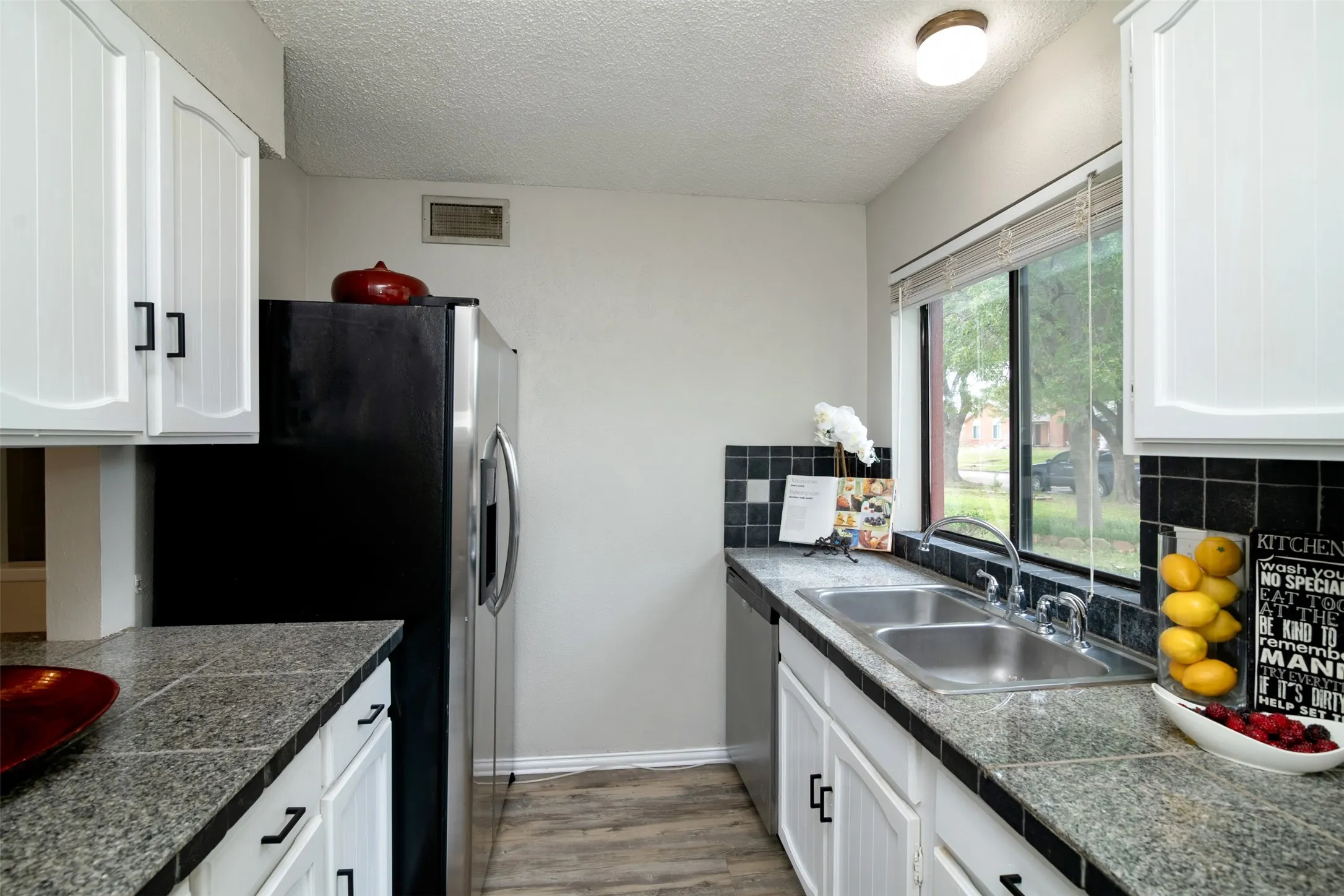 Galley kitchen featuring white cabinetry, granite-style countertops, a stainless steel double basin sink, and wood-finish flooring
