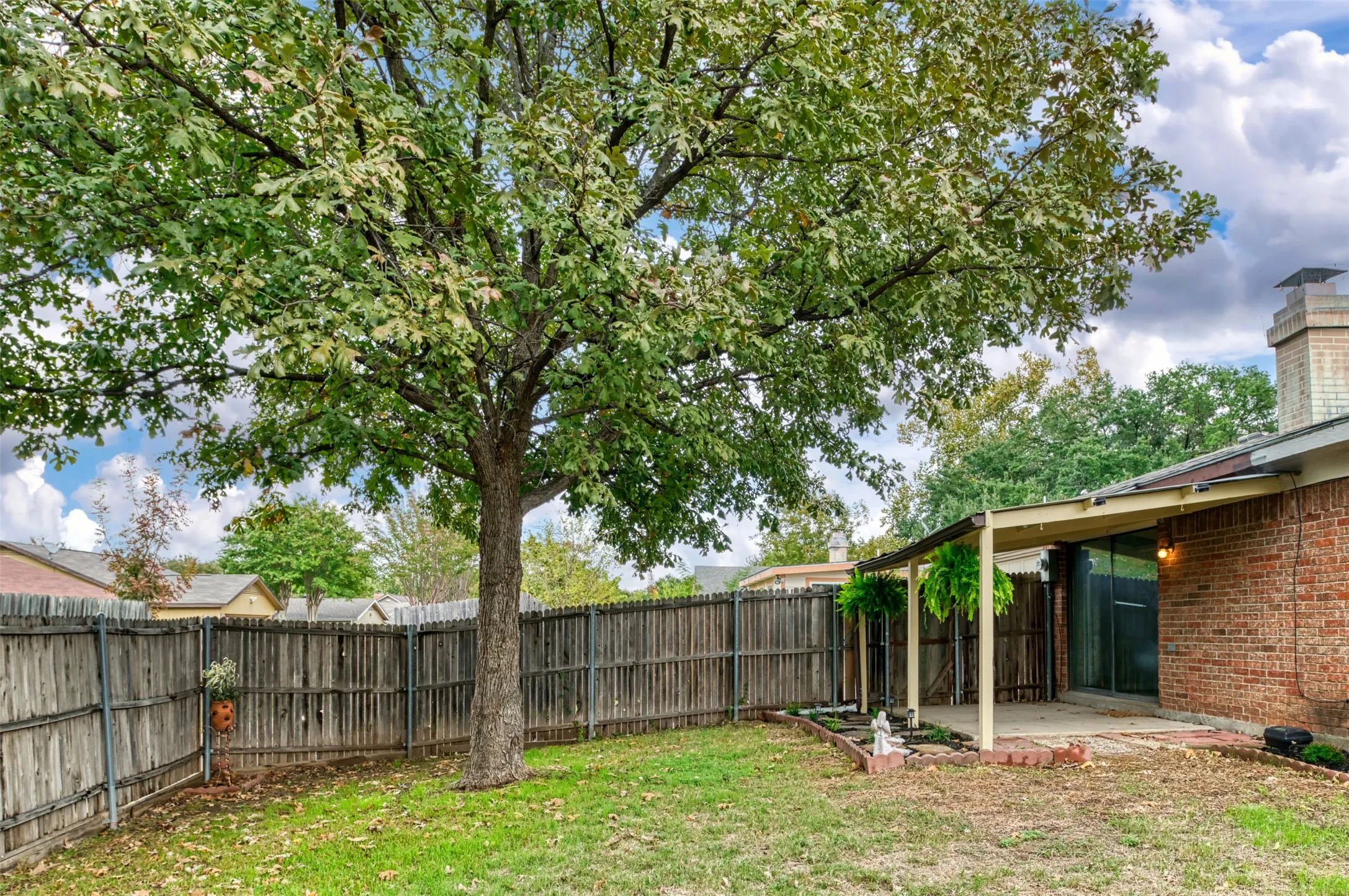 Fenced backyard with mature tree, brick exterior, and covered patio