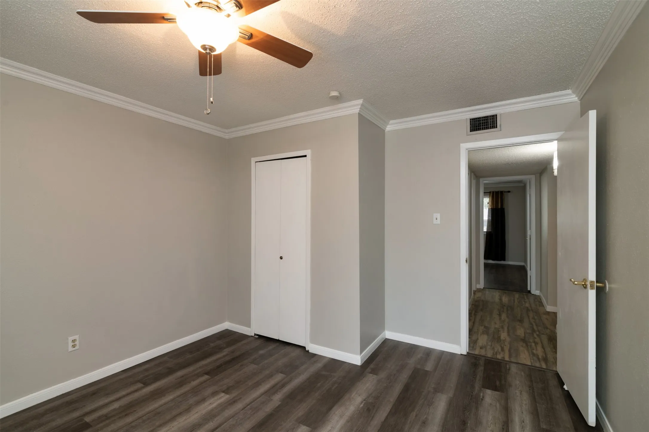 Wood-finish flooring, crown molding, ceiling fan with integrated lighting, and a bi-fold closet door