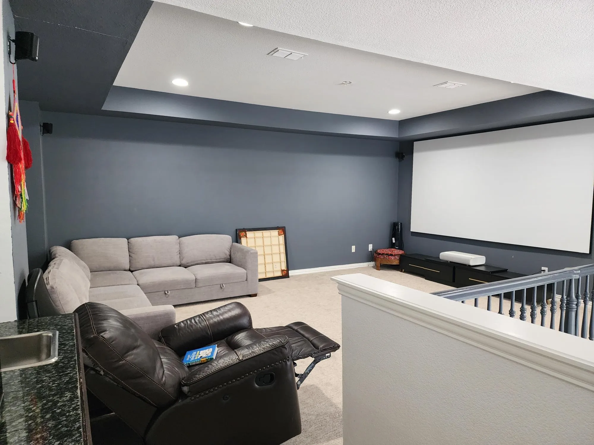 Spacious media room featuring a large projector screen, recessed lighting, and a built-in wet bar with a stainless steel sink and dark countertop