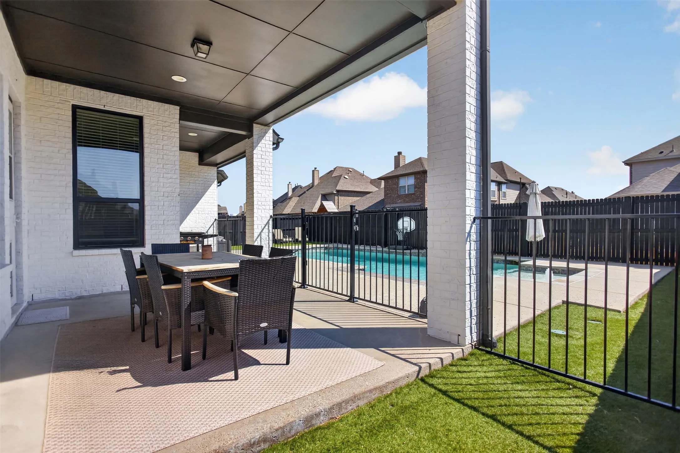 Covered patio with a dark paneled ceiling, white brick exterior, black frame windows, and a fenced swimming pool