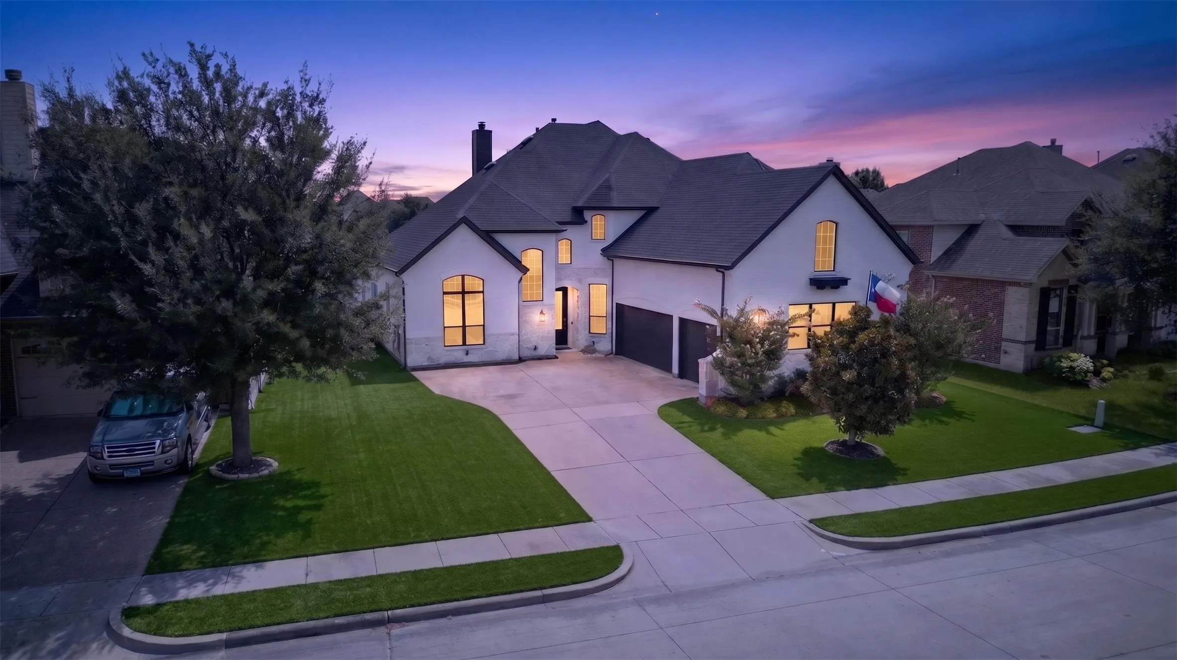 Stucco and stone exterior, arched windows, attached garage, concrete driveway, and manicured lawn