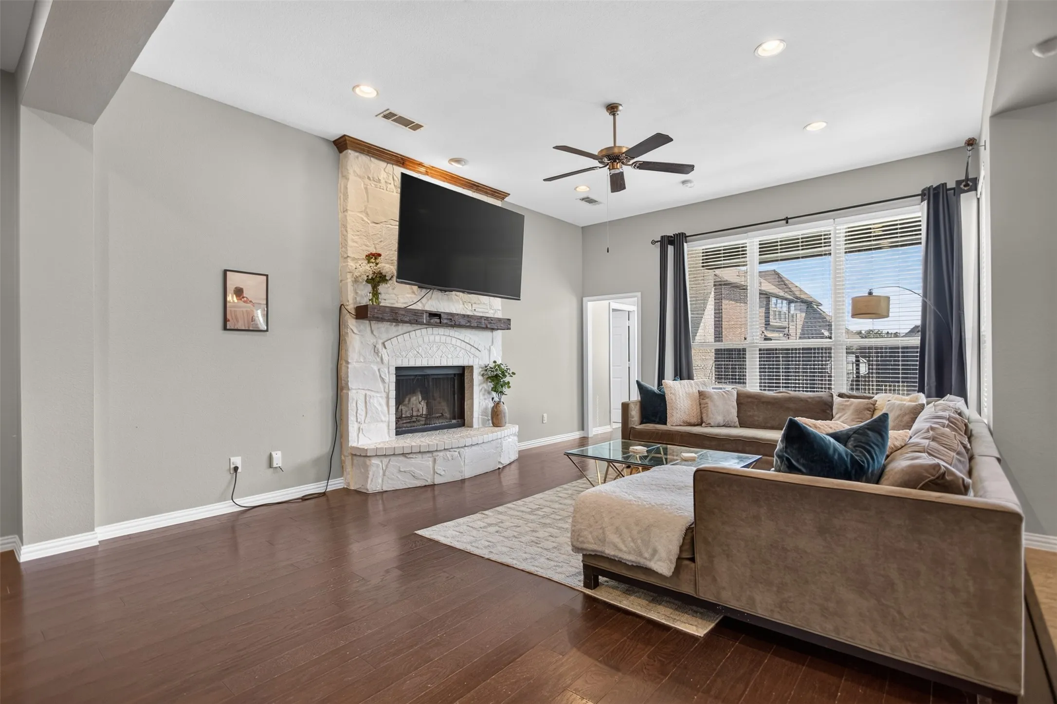 Spacious living area featuring dark wood-finish flooring, a stone-clad fireplace with a wood mantle, large windows, and recessed lighting