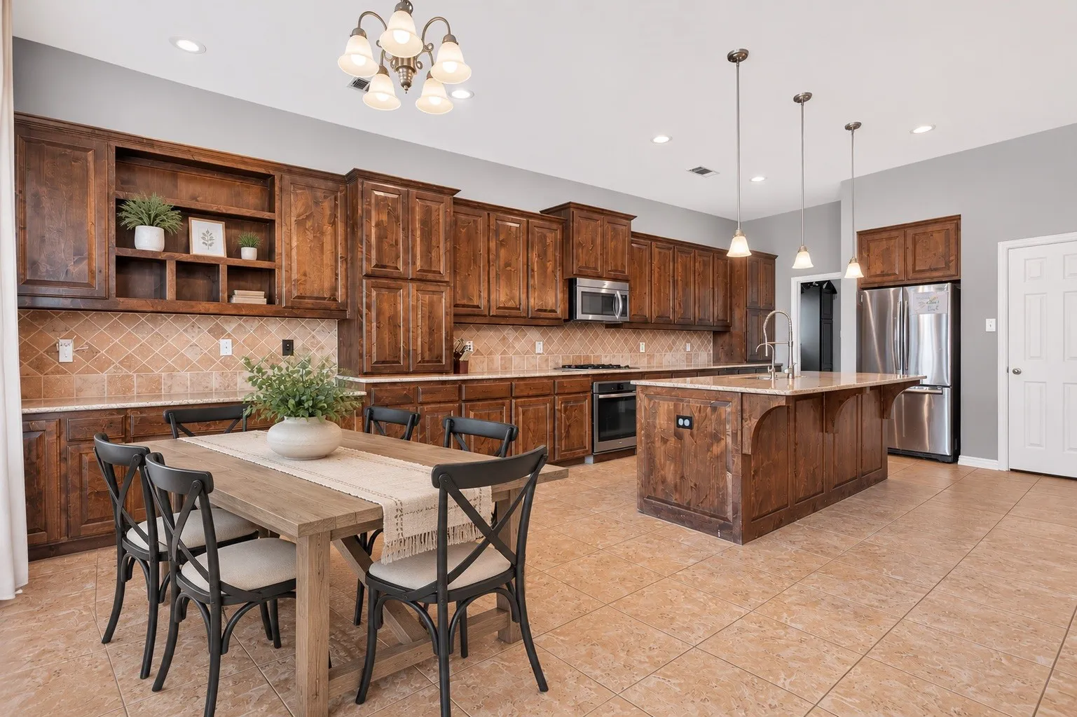 Expansive kitchen featuring wood cabinetry, stainless steel appliances, a large center island with a sink, and a tiled backsplash