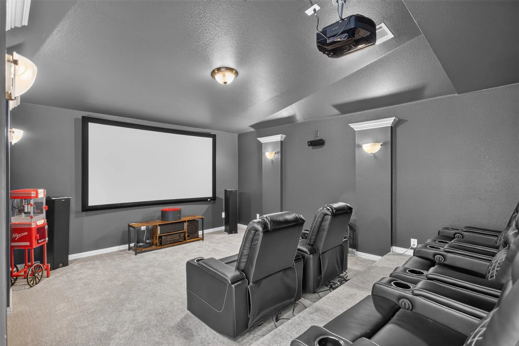 Dedicated home theater featuring a large projection screen, mounted projector, and sconce lighting