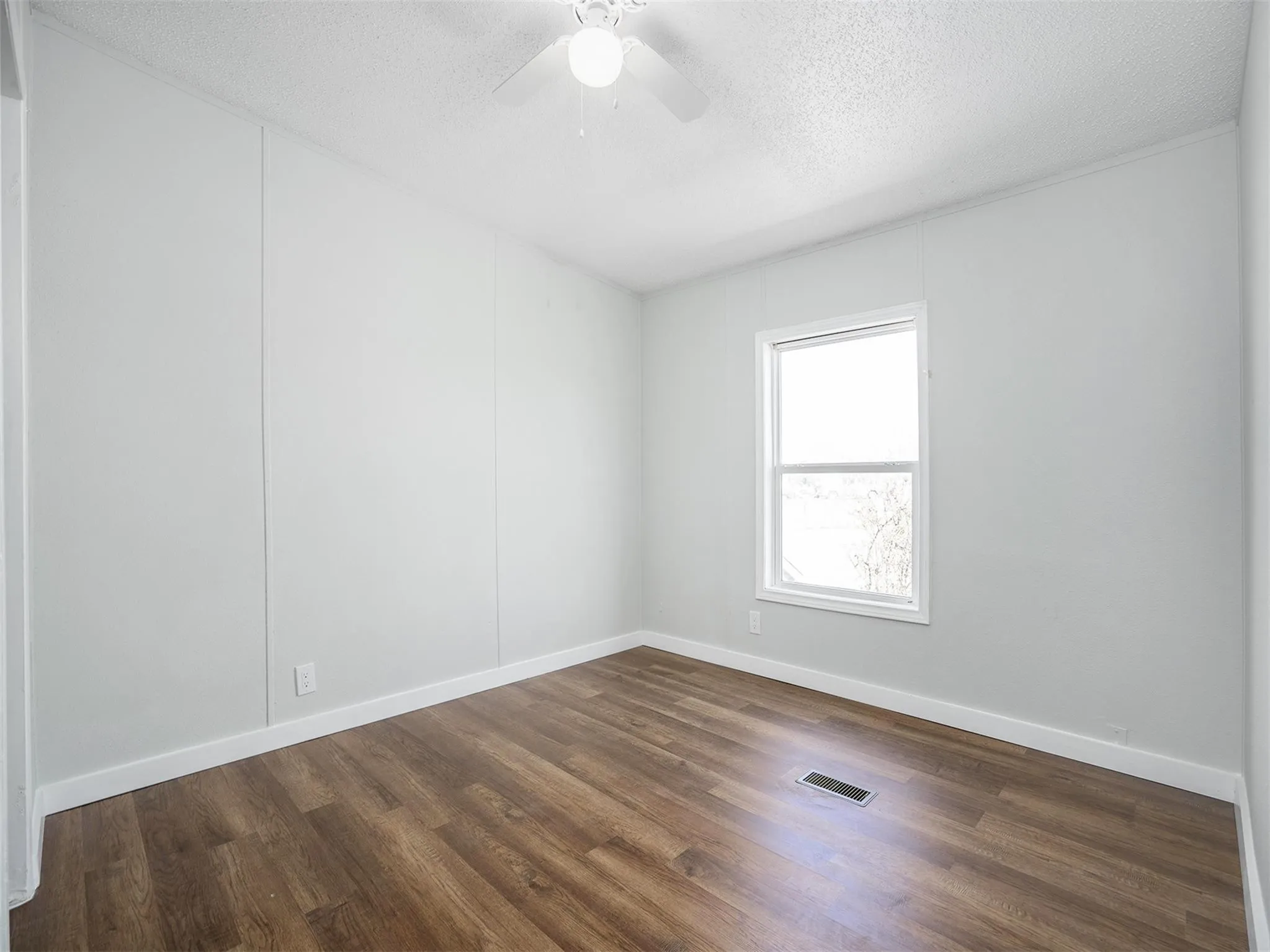 Empty room featuring a textured ceiling, dark wood-style floors, and a ceiling fan