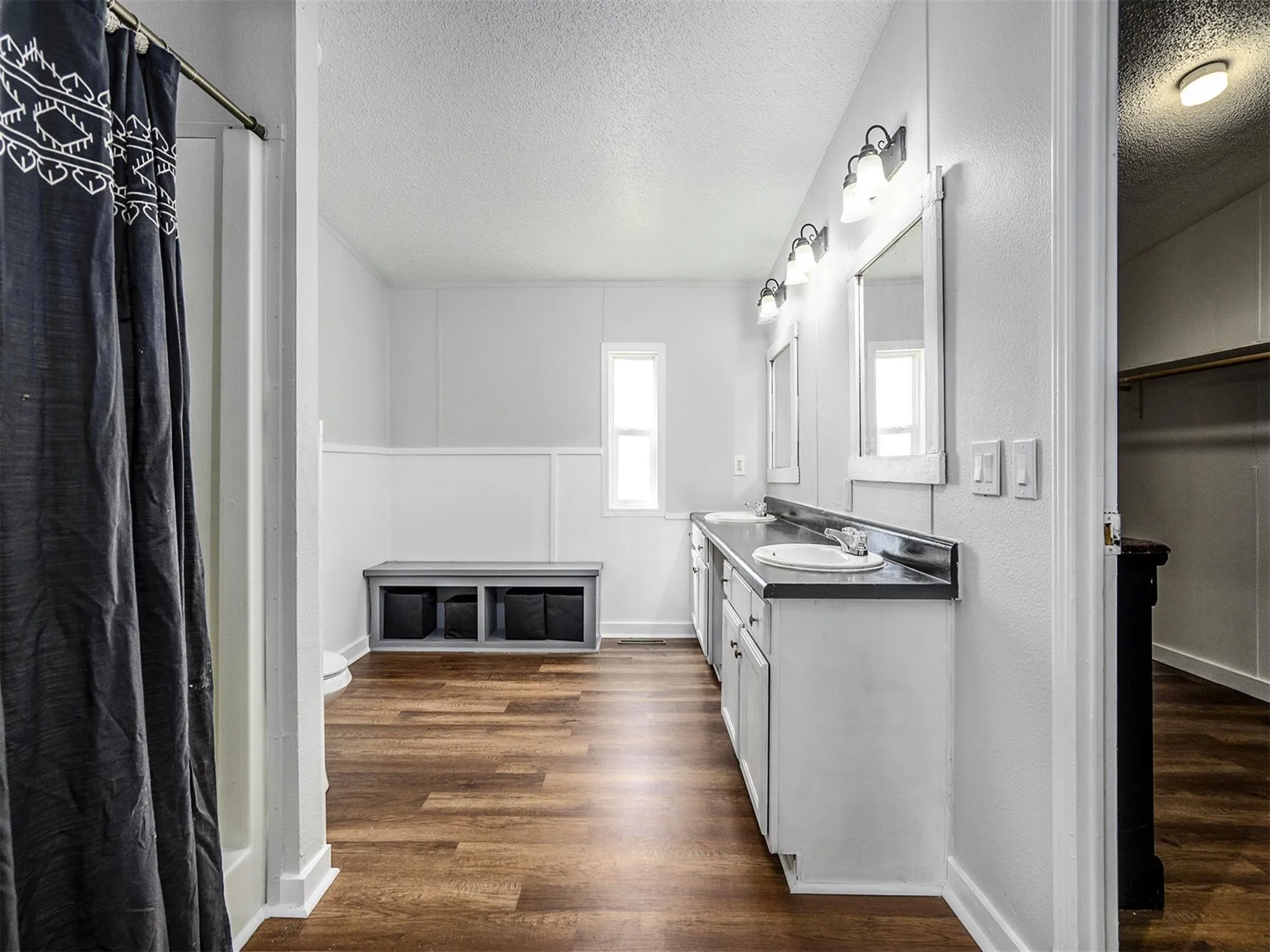 Bathroom featuring double vanity, dark wood-style floors, a textured ceiling, a spacious closet, and a shower with curtain