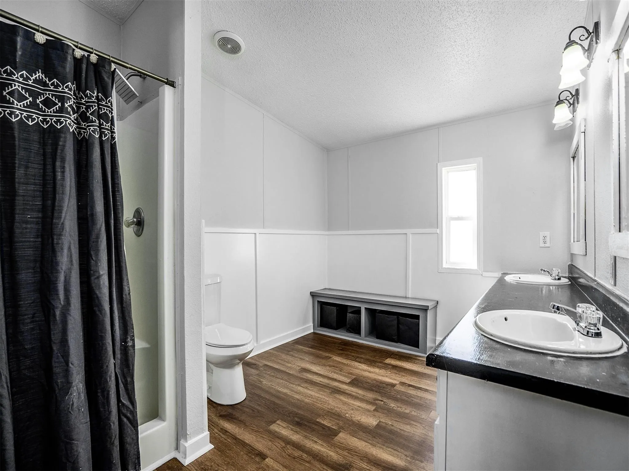 Bathroom featuring a textured ceiling, a stall shower, double vanity, and dark wood-type flooring