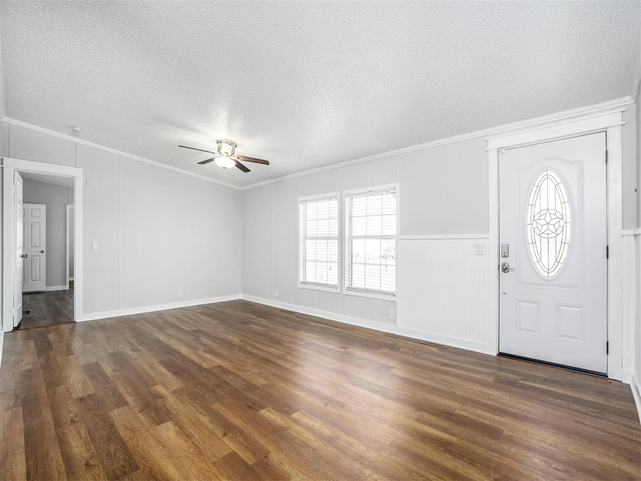 Entryway featuring a textured ceiling, dark wood-style flooring, crown molding, a ceiling fan, and wainscoting