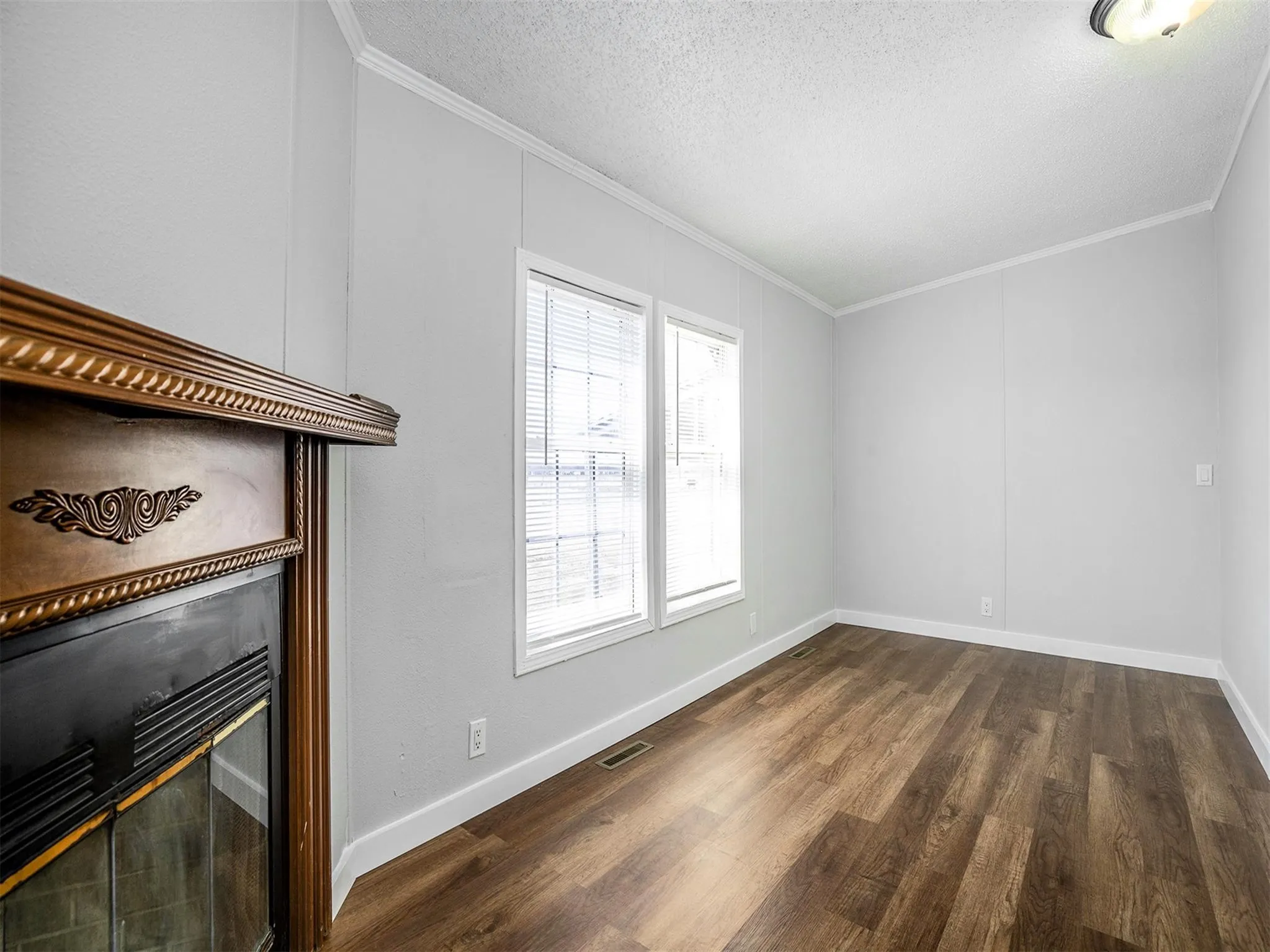 Unfurnished living room featuring ornamental molding, a textured ceiling, dark wood-style floors, and a glass covered fireplace