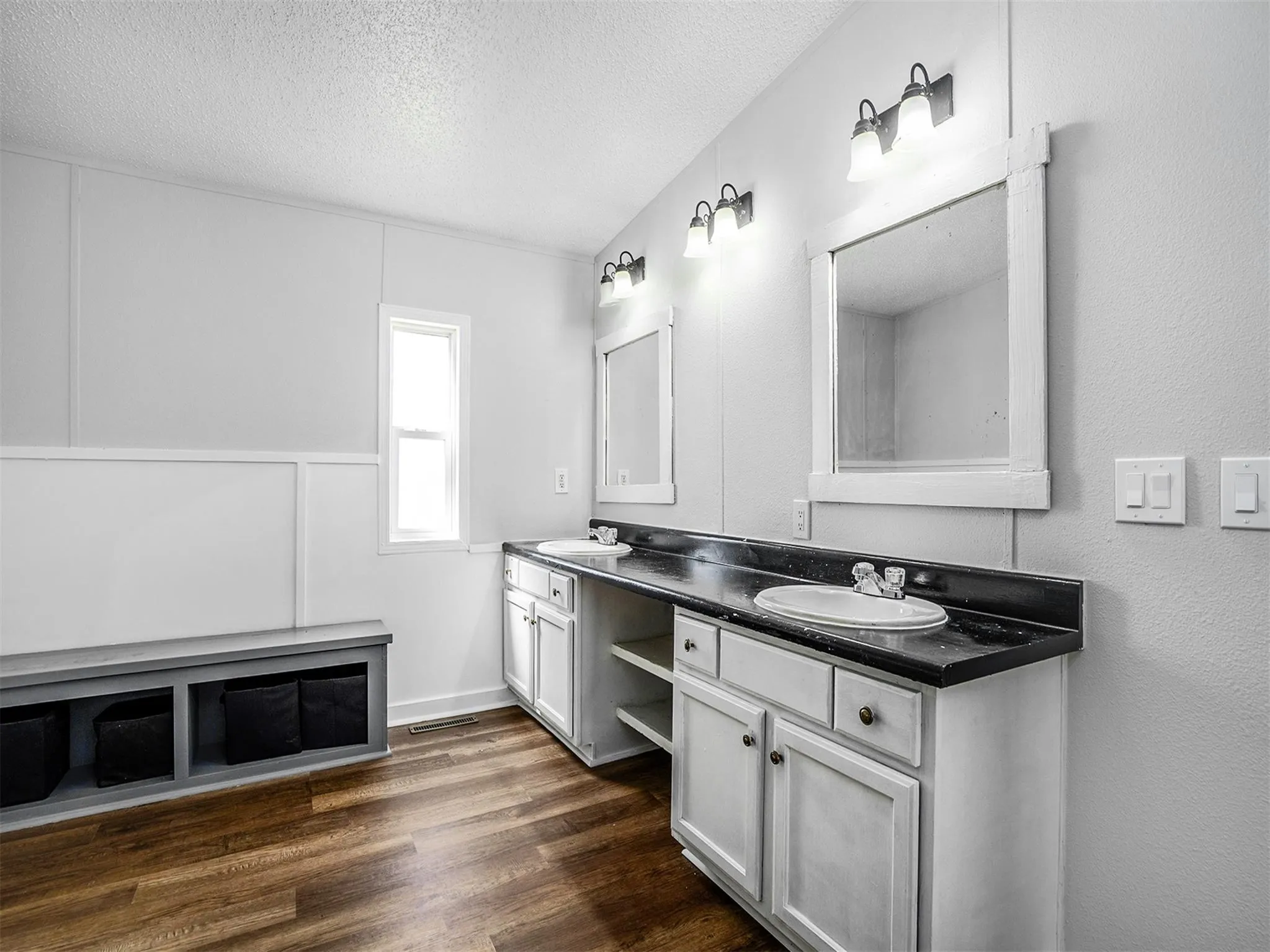 Full bath featuring double vanity, a textured ceiling, dark wood-type flooring, and a decorative wall