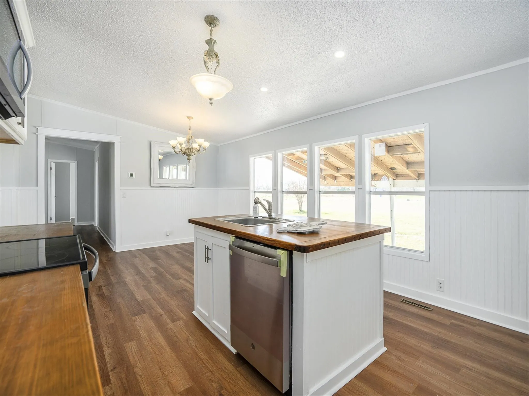 Kitchen with butcher block counters, wainscoting, pendant lighting, white cabinets, and appliances with stainless steel finishes