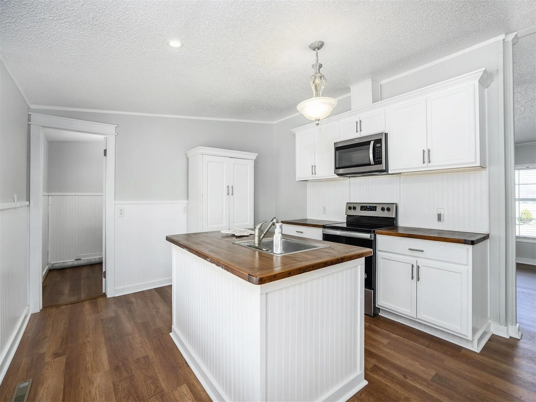 Kitchen with appliances with stainless steel finishes, white cabinetry, wood counters, an island with sink, and a textured ceiling