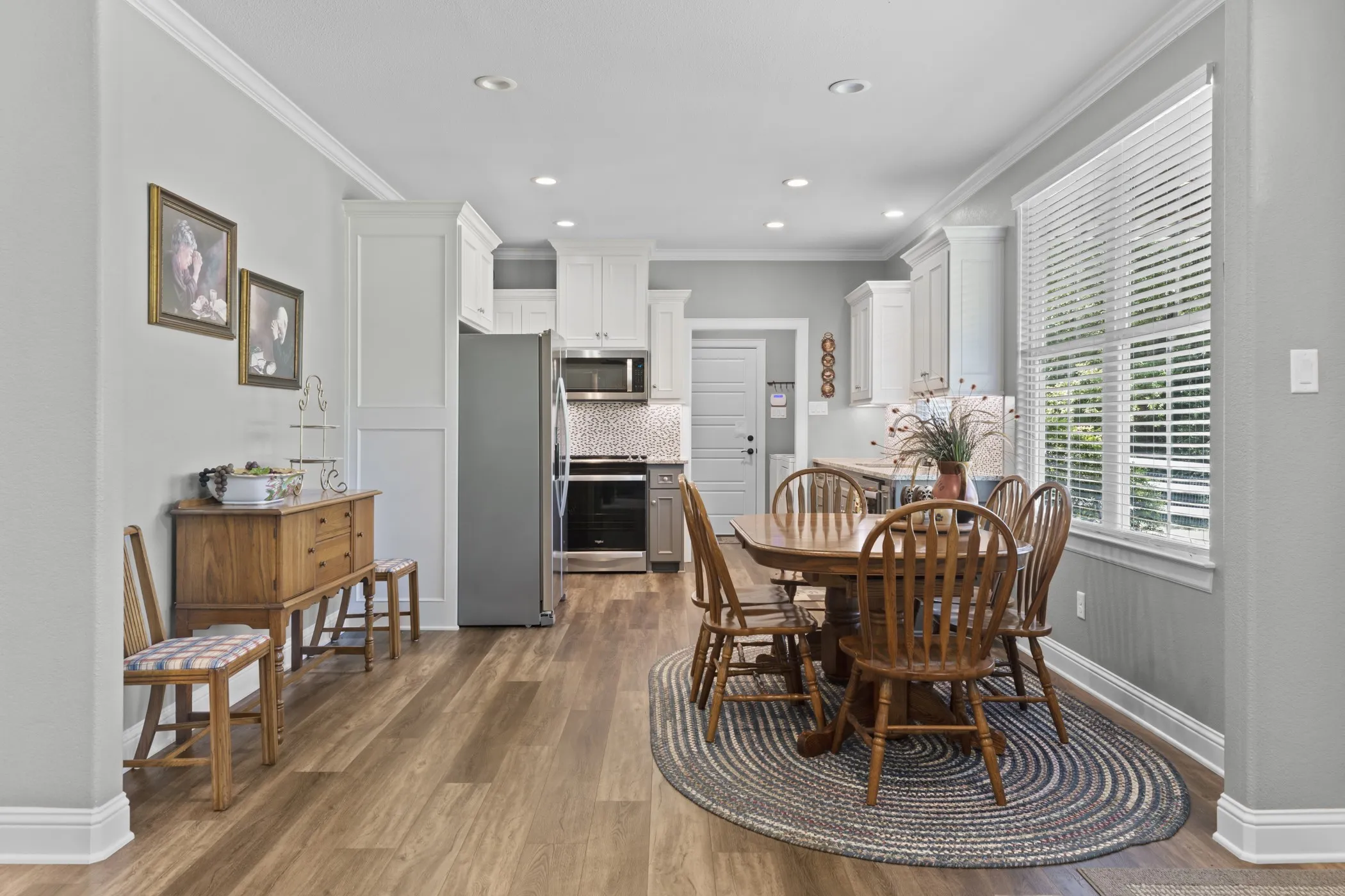 Kitchen and dining area featuring wood-finish flooring, white cabinetry, recessed lighting, and a stainless steel refrigerator