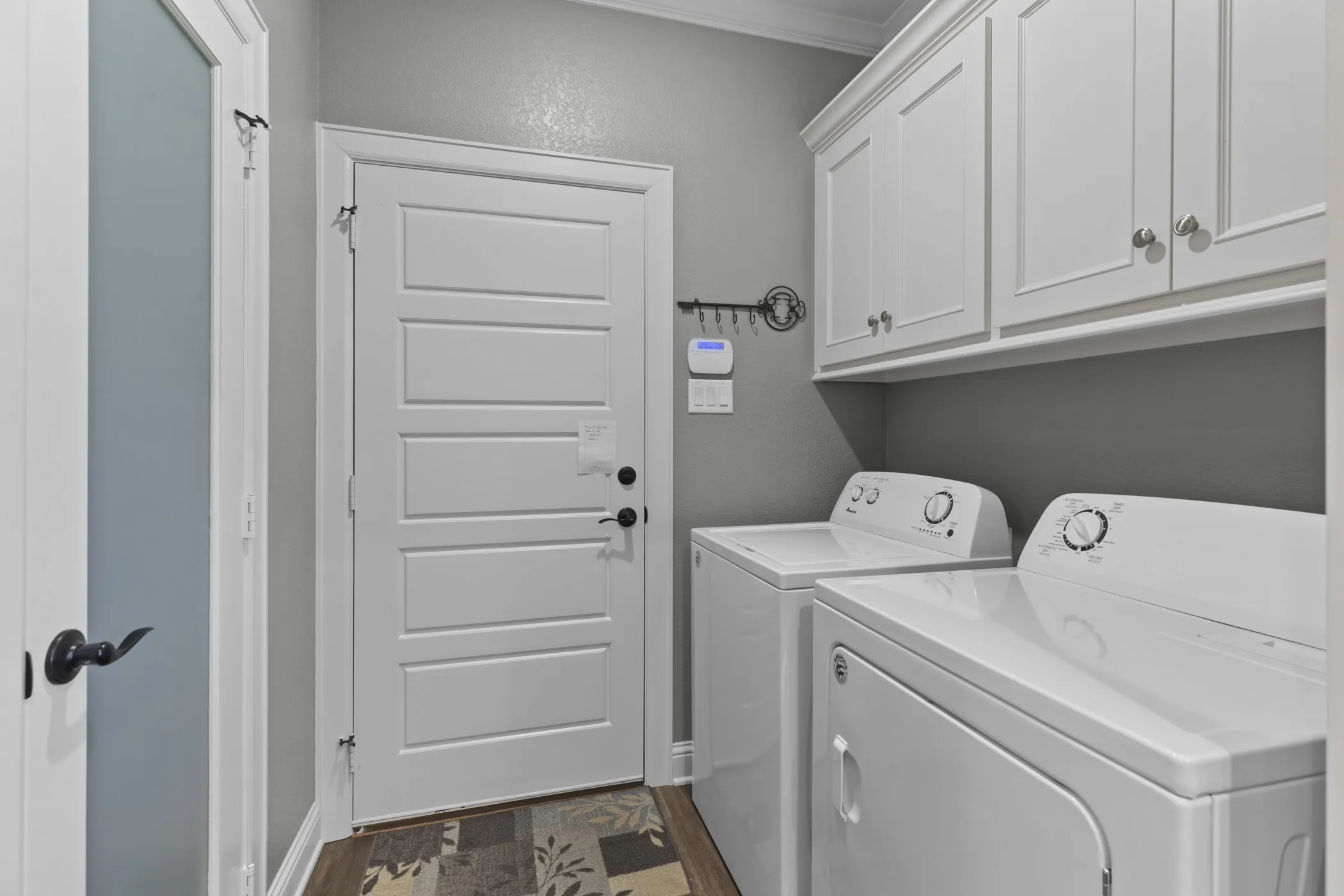 White shaker-style cabinetry with crown molding, solid-core interior door, and wood-finish flooring