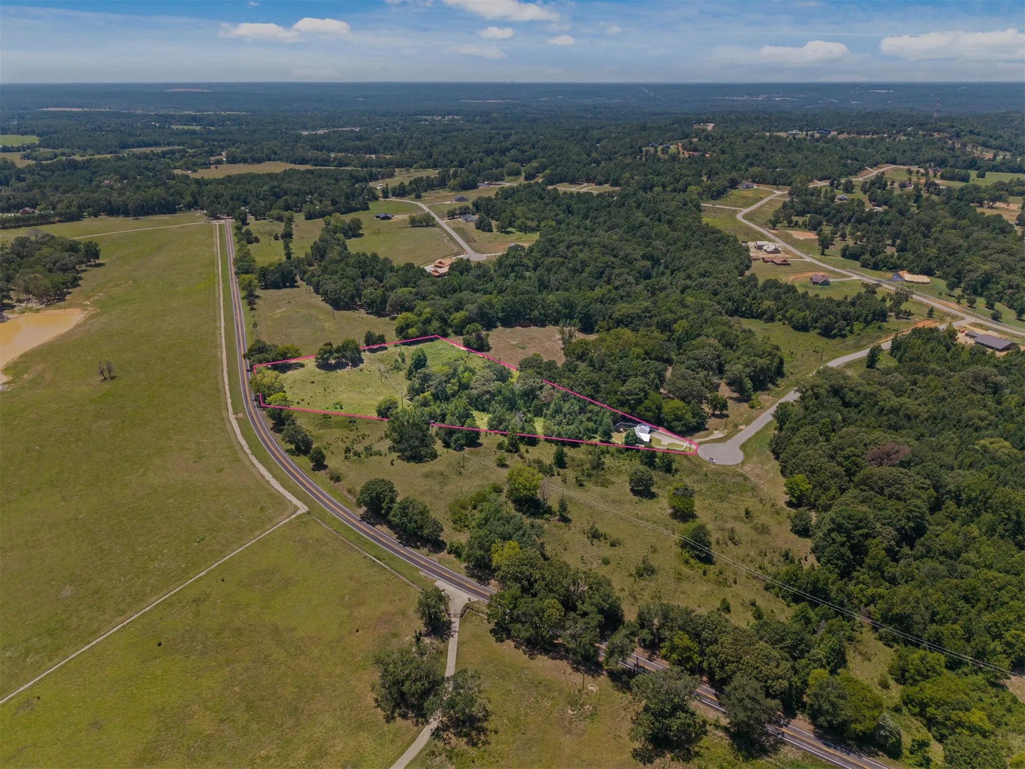 Expansive property featuring a mix of open fields and mature trees, with a visible railroad track running alongside