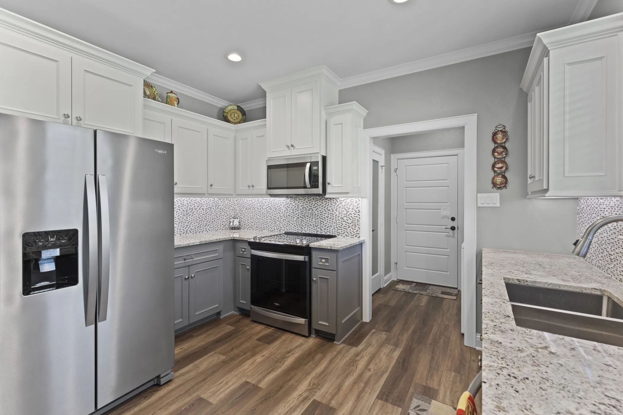 Kitchen featuring wood-finish flooring, two-tone cabinetry, stainless steel appliances, granite countertops, and a mosaic tile backsplash
