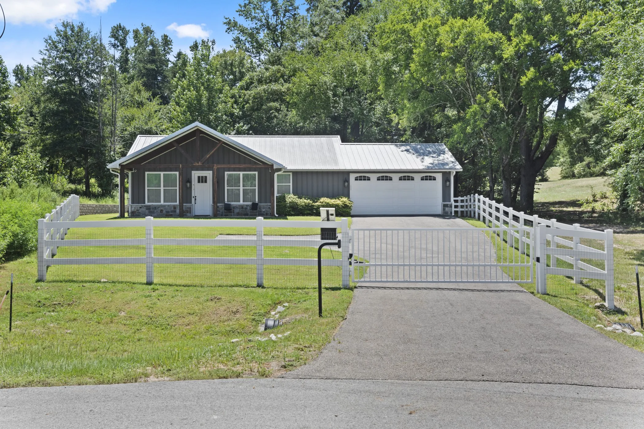 Gated asphalt driveway with a white three-rail fence