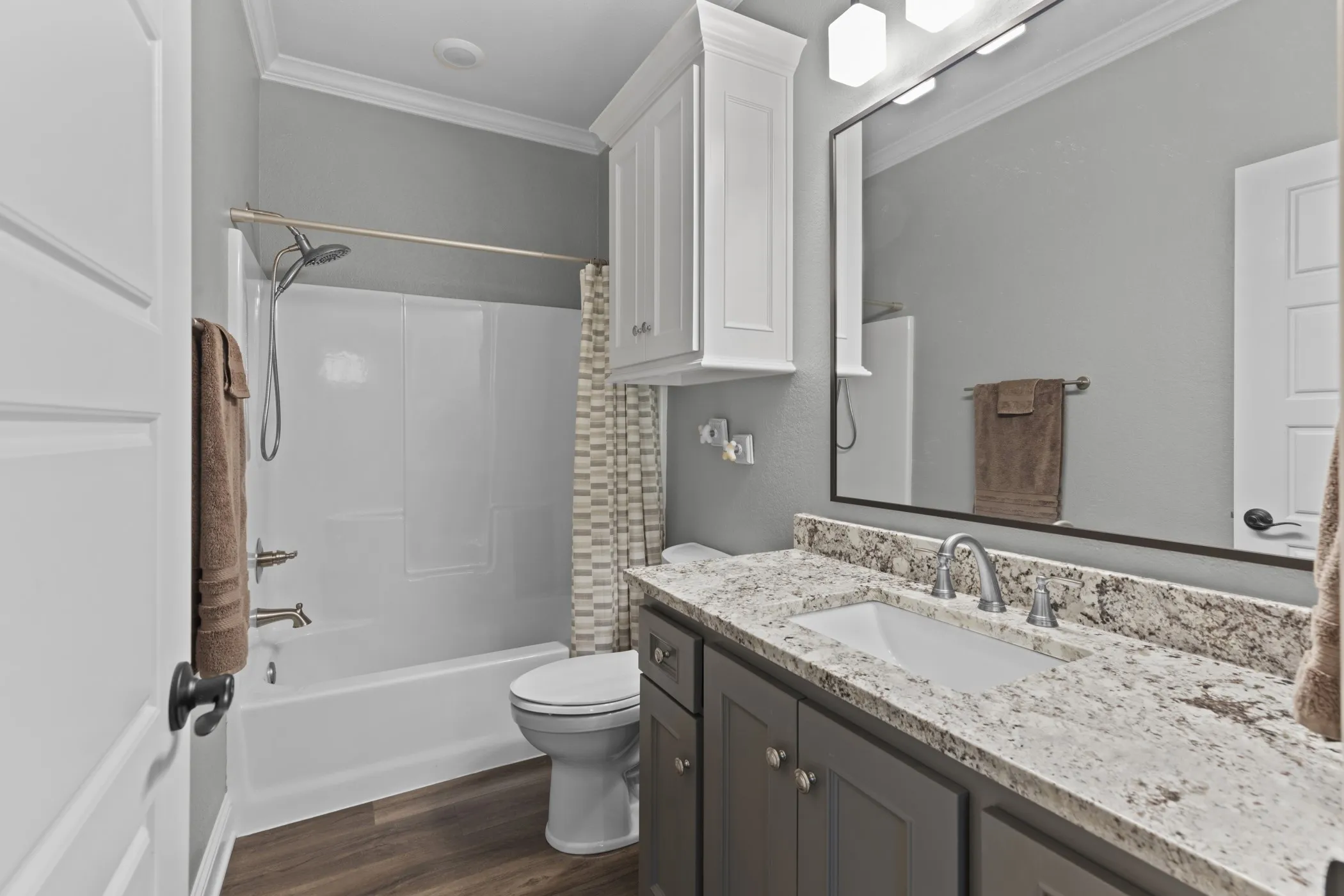 Bathroom featuring a bathtub with shower, wood-finish flooring, white cabinetry, a vanity with an undermount sink, and a large mirror