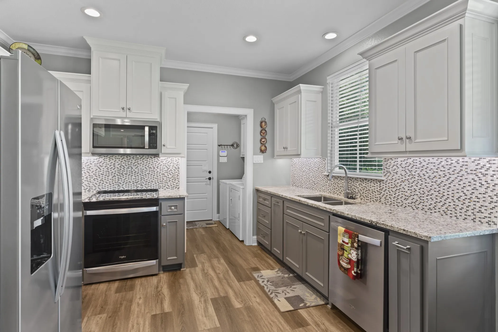 Kitchen featuring two-tone cabinetry, stainless steel appliances, granite countertops, and a mosaic tile backsplash