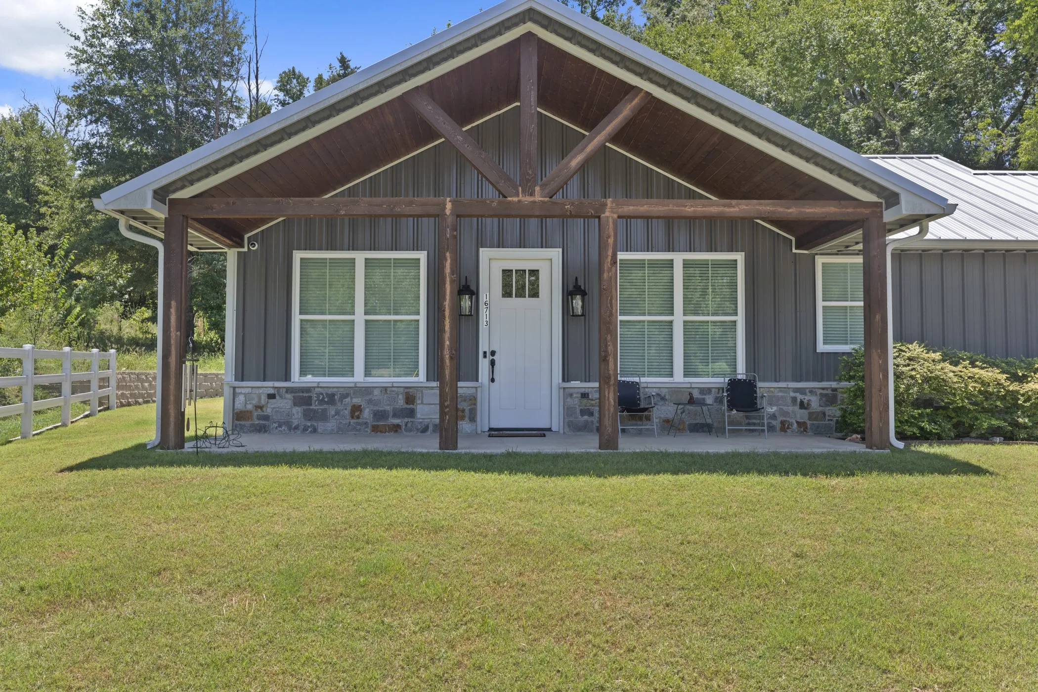 Covered porch with exposed wood beams, board and batten siding, stone veneer accents, white paneled entry door, and a metal roof