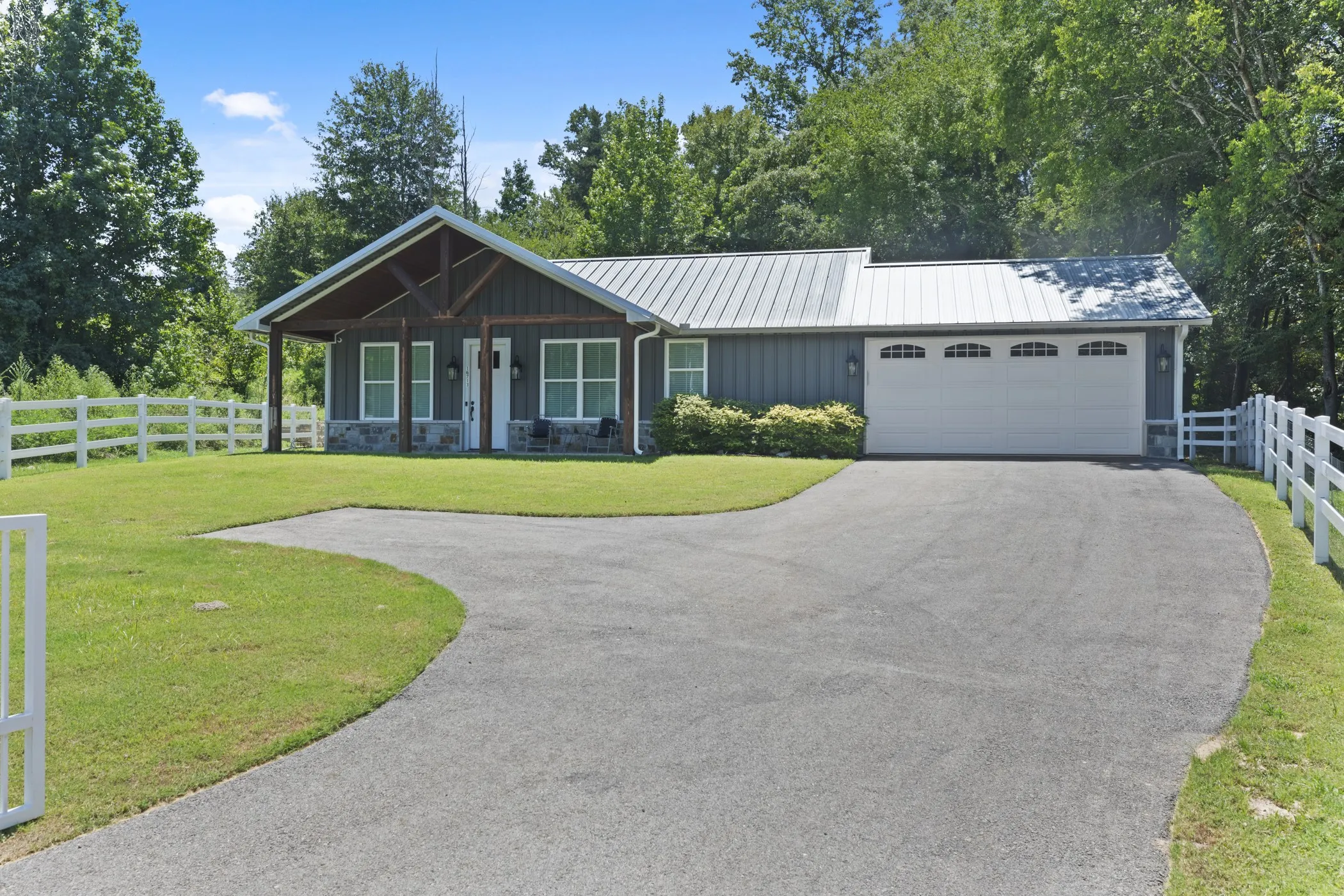 Ranch-style exterior with a covered front porch, stone accents, metal roof, and an attached two-car garage