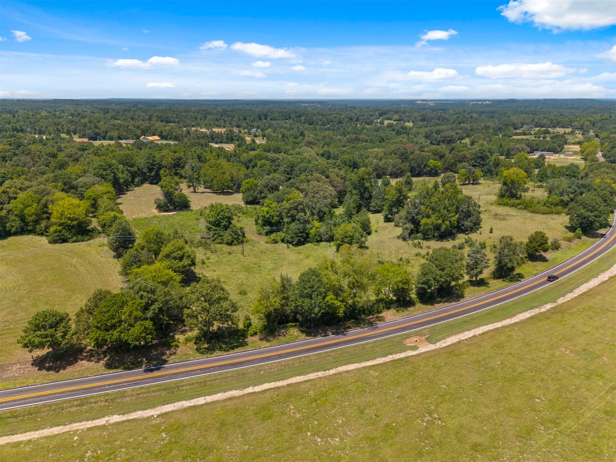 Expansive acreage featuring a paved roadway and surrounding woodlands