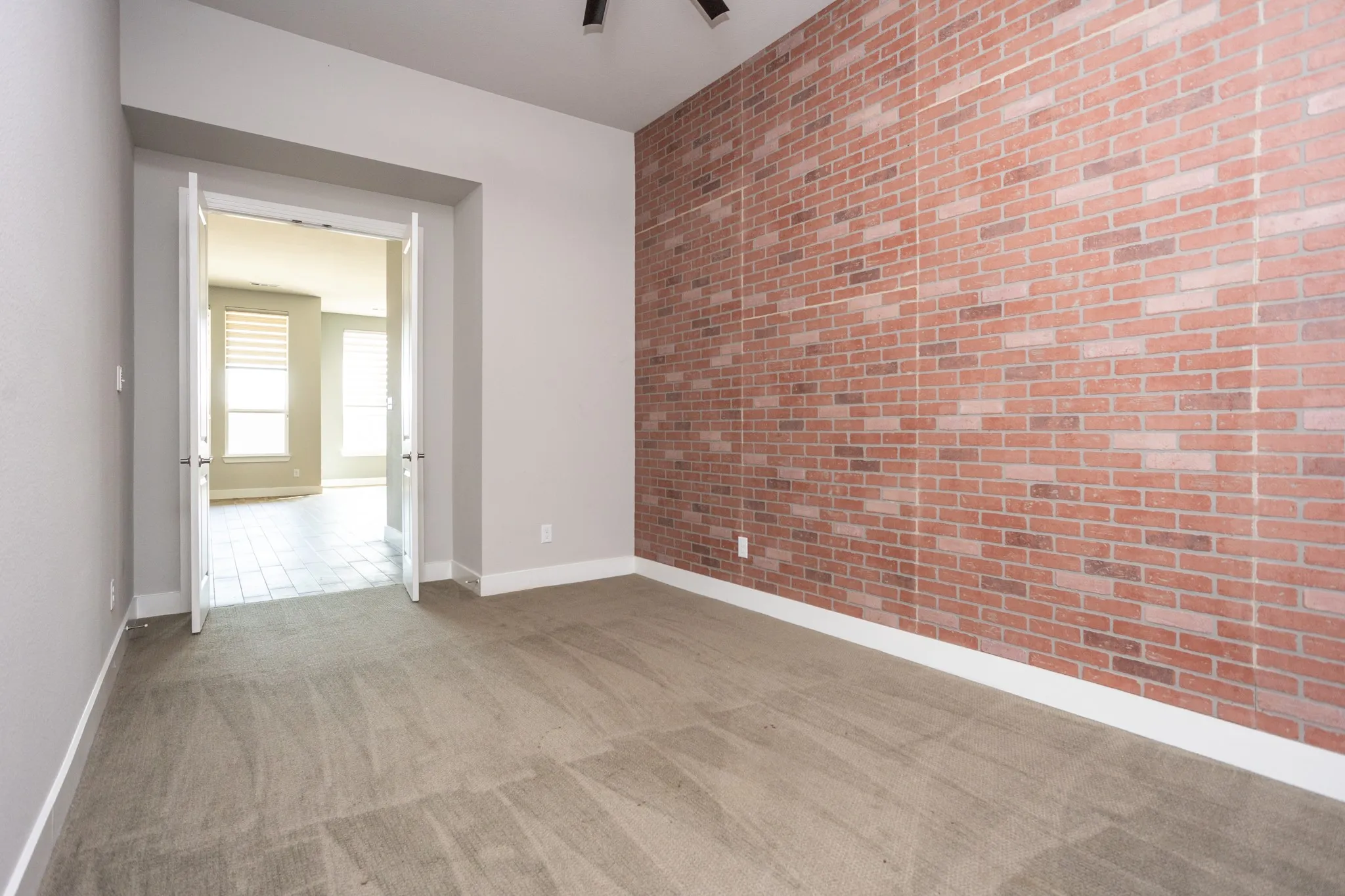 Brick accent wall, carpeted flooring, double French doors, light gray wall paint, white trim