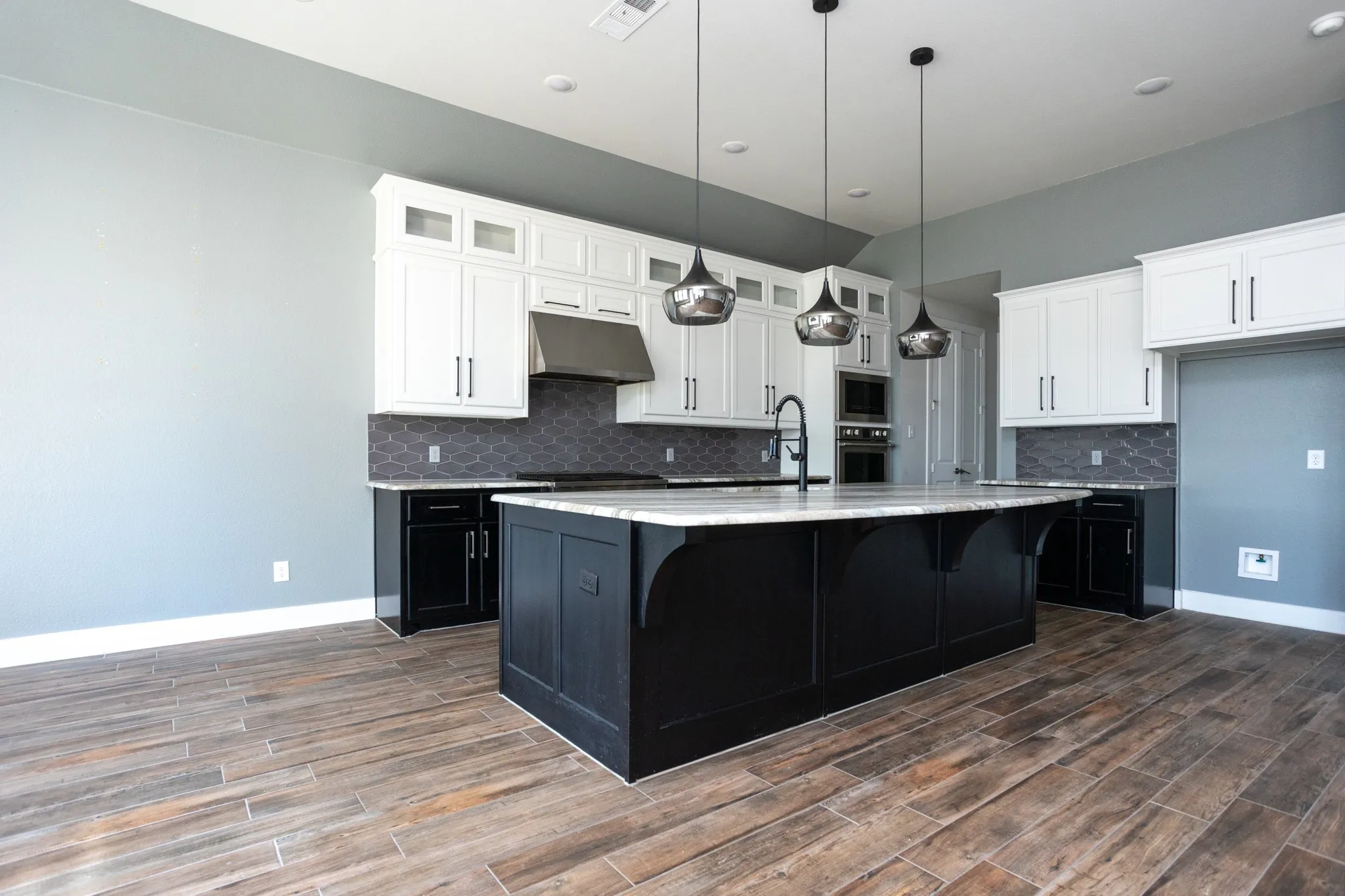 Spacious kitchen featuring an expansive center island with seating, white cabinetry, dark lower cabinetry, and wood-finish flooring
