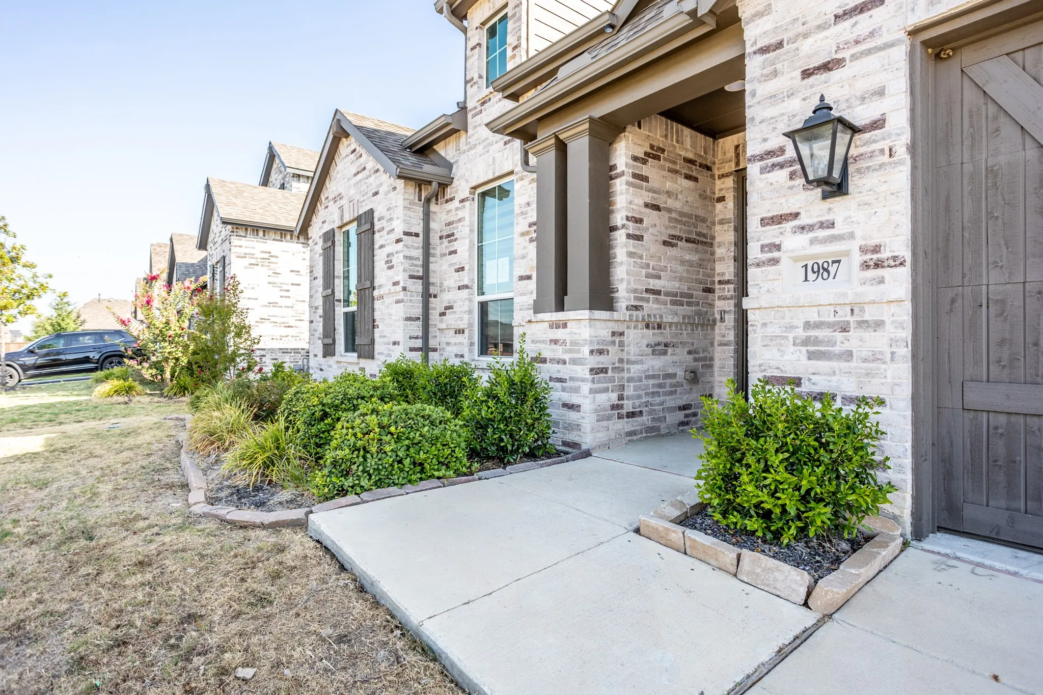 Brick exterior with stone accents, covered entry, decorative exterior lighting, and a wood-finish garage door